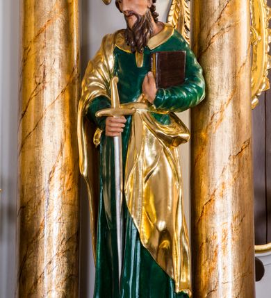 Zdjęcie nr 2: Drążona z tyłu, całopostaciowa figura przedstawia św. Pawła stojącego na niewysokiej podstawie, zwróconego na wprost. Skierowaną w trzech czwartych w prawo głowę charakteryzuje pociągła twarz o wyrazistych, sumarycznie opracowanych rysach z długim spiczastym nosem, wystającymi kośćmi policzkowymi oraz długim zarostem. Lekko skręcone, zebrane do tyłu włosy sięgają ramion. Święty ubrany jest w ciemnozieloną suknię ze złoconymi paskiem i kołnierzem oraz złocony płaszcz narzucony na prawe ramię i podwinięty pod pasek. W prawej ręce trzyma złocono-srebrzony miecz skierowany ostrzem w dół, lewą przyciska do piersi zamkniętą księgę w brązowej oprawie.     