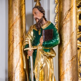 Zdjęcie nr 1: Drążona z tyłu, całopostaciowa figura przedstawia św. Pawła stojącego na niewysokiej podstawie, zwróconego na wprost. Skierowaną w trzech czwartych w prawo głowę charakteryzuje pociągła twarz o wyrazistych, sumarycznie opracowanych rysach z długim spiczastym nosem, wystającymi kośćmi policzkowymi oraz długim zarostem. Lekko skręcone, zebrane do tyłu włosy sięgają ramion. Święty ubrany jest w ciemnozieloną suknię ze złoconymi paskiem i kołnierzem oraz złocony płaszcz narzucony na prawe ramię i podwinięty pod pasek. W prawej ręce trzyma złocono-srebrzony miecz skierowany ostrzem w dół, lewą przyciska do piersi zamkniętą księgę w brązowej oprawie.     