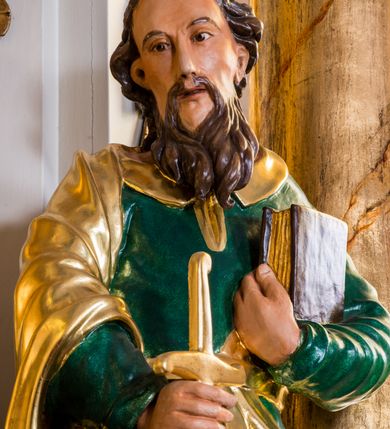 Zdjęcie nr 5: Drążona z tyłu, całopostaciowa figura przedstawia św. Pawła stojącego na niewysokiej podstawie, zwróconego na wprost. Skierowaną w trzech czwartych w prawo głowę charakteryzuje pociągła twarz o wyrazistych, sumarycznie opracowanych rysach z długim spiczastym nosem, wystającymi kośćmi policzkowymi oraz długim zarostem. Lekko skręcone, zebrane do tyłu włosy sięgają ramion. Święty ubrany jest w ciemnozieloną suknię ze złoconymi paskiem i kołnierzem oraz złocony płaszcz narzucony na prawe ramię i podwinięty pod pasek. W prawej ręce trzyma złocono-srebrzony miecz skierowany ostrzem w dół, lewą przyciska do piersi zamkniętą księgę w brązowej oprawie.     