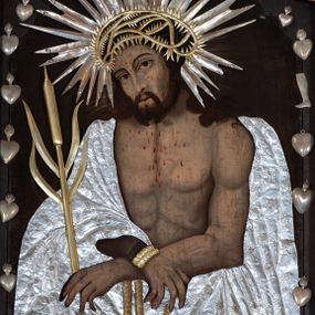 Zdjęcie nr 1: Obraz w formie stojącego prostokąta zamkniętego łukiem półkolistym nadwieszonym z uskokiem. W centrum Chrystus ukazany w półpostaci, zwrócony w trzech czwartych w prawo, z pochyloną głową i skrzyżowanymi dłońmi, związanymi w nadgarstkach powrozem. Twarz ma pociągłą, ze śladami krwi, o dużych, migdałowatych oczach, lekko garbatym nosie oraz pełnych, rozchylonych ustach z widoczną linią zębów; okoloną krótką, rozdwajającą się brodą oraz długimi, silnie kręconymi włosami opadającymi na ramiona. Na głowę ma nałożoną metalową, złoconą koronę cierniową, a wokół metalową, srebrzoną glorię promienistą. Chrystus na ramiona ma narzucony płaszcz odsłaniający tors, na który nałożono metalową, srebrzoną sukienkę, o drobnym, kwiecistym wzorze. Ciało szczupłe, o podkreślonej muskulaturze, z zaznaczonymi śladami krwi. Na nadgarstki ma nałożony metalowy, złocony powróz, w lewej ręce trzyma trzcinę, na którą nałożona jest metalowa, złocona. Chrystus ukazany jest na ciemnobrązowym tle, wokół postaci zawieszone wota.



