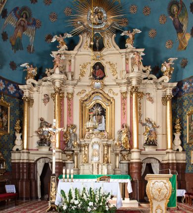 Zdjęcie nr 13: Nastawa ołtarzowa architektoniczna, dwukondygnacyjna, ze zwieńczeniem, pierwsza kondygnacja trójosiowa, druga jednoosiowa, ustawiona na dwustrefowym cokole z wyodrębnionymi, cylindrycznymi fragmentami, z bramkami na osiach bocznych. Ołtarz prostopadłościenny, murowany, z kamienną mensą i kamiennym portatylem. 
Pierwsza kondygnacja wydzielona czterema parami wklęsłych pilastrów o trzonach dekorowanych rocaille'em i zwisami kwiatowymi oraz stojącymi na ich tle dwiema parami kolumn o kapitelach kompozytowych. Podpory dźwigają niepełne belkowanie, przerwane nad polami kondygnacji, obniżone nad zewnętrzną parą kolumn. Na skrajnej partii cokołu nastawy karbowane woluty z fantazyjnymi gruszkowatymi cokołami podtrzymującymi rocaille'owe wazony. W polu środkowym głęboka wnęka w formie stojącego prostokąta zamkniętego łukiem odcinkowym podwójnie nadwieszonym z uskokiem, ujęta profilowaną ramą, z obrazem Ecce Homo w osobnej, podwójnej ramie. Nad nią kartusz rokokowy z napisem „In nomine Jesu / om(n)e Genu flec / tatur. ad Philipenses / Cap(ut) II”. Wnękę flankują figury Matki Boskiej i św. Marii Magdaleny ustawione na rocaille'owych konsolach. Na osiach bocznych figura Dawida i grupa ofiary Izaaka na cokołach z nadlatującymi puttami nad nimi. Druga kondygnacja flankowana trzema parami pilastrów o trzonach przechodzących w spływy wolutowe i osobne woluty, opadające na belkowanie pierwszej kondygnacji, na których siedzą putta i anioły trzymające kartusze z napisami: „ET / GLORIA” i „SOLI / DEO / HONOR”. Kondygnacja zamknięta profilowanym gzymsem wyłamanym na ich osi oraz załamanym w dół nad polem. Na gzymsie fragmenty przerwanego, falistego przyczółka, na których siedzą anioły. W polu obraz św. Macieja w formie zbliżonej do trapezu o dwóch wypukłych bokach, ujęty profilowaną ramą. Pole flankowane akantem, powyżej rocaille'owy kartusz z napisem: „IN / CRUCE / SALUS”. Zwieńczenie w formie zbliżonej do trapezu, o wklęsłych bokach, ujętych wolutami, zamknięte cęgowymi wolutami. W polu obraz Ukrzyżowania w formie zbliżonej do trapezu o dwóch wypukłych bokach, ujęty profilowaną ramą, flankowany akantem. Całość zamknięta płaskorzeźbionym przedstawieniem popiersia Boga Ojca oraz gołębicy Ducha Świętego w glorii, w otoku z obłoków i uskrzydlonych główek anielskich, w glorii promienistej, u dołu szarfa z napisem: „Hic est Filius meus dilectus in quo mihi bene complacui ipsum audite. Luc[a] XVII”. Struktura polichromowana w kolorze beżowym, dolna strefa cokołu brązowa, część trzonów pilastrów pomalowana na kolor jasnoróżowy; trzony kolumn, profile i ornamentyka złocone, detal srebrzony.  


