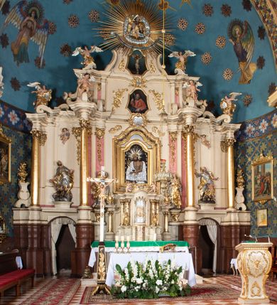 Zdjęcie nr 24: Nastawa ołtarzowa architektoniczna, dwukondygnacyjna, ze zwieńczeniem, pierwsza kondygnacja trójosiowa, druga jednoosiowa, ustawiona na dwustrefowym cokole z wyodrębnionymi, cylindrycznymi fragmentami, z bramkami na osiach bocznych. Ołtarz prostopadłościenny, murowany, z kamienną mensą i kamiennym portatylem. 
Pierwsza kondygnacja wydzielona czterema parami wklęsłych pilastrów o trzonach dekorowanych rocaille'em i zwisami kwiatowymi oraz stojącymi na ich tle dwiema parami kolumn o kapitelach kompozytowych. Podpory dźwigają niepełne belkowanie, przerwane nad polami kondygnacji, obniżone nad zewnętrzną parą kolumn. Na skrajnej partii cokołu nastawy karbowane woluty z fantazyjnymi gruszkowatymi cokołami podtrzymującymi rocaille'owe wazony. W polu środkowym głęboka wnęka w formie stojącego prostokąta zamkniętego łukiem odcinkowym podwójnie nadwieszonym z uskokiem, ujęta profilowaną ramą, z obrazem Ecce Homo w osobnej, podwójnej ramie. Nad nią kartusz rokokowy z napisem „In nomine Jesu / om(n)e Genu flec / tatur. ad Philipenses / Cap(ut) II”. Wnękę flankują figury Matki Boskiej i św. Marii Magdaleny ustawione na rocaille'owych konsolach. Na osiach bocznych figura Dawida i grupa ofiary Izaaka na cokołach z nadlatującymi puttami nad nimi. Druga kondygnacja flankowana trzema parami pilastrów o trzonach przechodzących w spływy wolutowe i osobne woluty, opadające na belkowanie pierwszej kondygnacji, na których siedzą putta i anioły trzymające kartusze z napisami: „ET / GLORIA” i „SOLI / DEO / HONOR”. Kondygnacja zamknięta profilowanym gzymsem wyłamanym na ich osi oraz załamanym w dół nad polem. Na gzymsie fragmenty przerwanego, falistego przyczółka, na których siedzą anioły. W polu obraz św. Macieja w formie zbliżonej do trapezu o dwóch wypukłych bokach, ujęty profilowaną ramą. Pole flankowane akantem, powyżej rocaille'owy kartusz z napisem: „IN / CRUCE / SALUS”. Zwieńczenie w formie zbliżonej do trapezu, o wklęsłych bokach, ujętych wolutami, zamknięte cęgowymi wolutami. W polu obraz Ukrzyżowania w formie zbliżonej do trapezu o dwóch wypukłych bokach, ujęty profilowaną ramą, flankowany akantem. Całość zamknięta płaskorzeźbionym przedstawieniem popiersia Boga Ojca oraz gołębicy Ducha Świętego w glorii, w otoku z obłoków i uskrzydlonych główek anielskich, w glorii promienistej, u dołu szarfa z napisem: „Hic est Filius meus dilectus in quo mihi bene complacui ipsum audite. Luc[a] XVII”. Struktura polichromowana w kolorze beżowym, dolna strefa cokołu brązowa, część trzonów pilastrów pomalowana na kolor jasnoróżowy; trzony kolumn, profile i ornamentyka złocone, detal srebrzony.  


