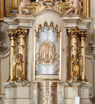 Zdjęcie nr 75: Nastawa ołtarzowa architektoniczna, dwukondygnacyjna, ze zwieńczeniem, pierwsza kondygnacja trójosiowa, druga jednoosiowa, ustawiona na dwustrefowym cokole z wyodrębnionymi, cylindrycznymi fragmentami, z bramkami na osiach bocznych. Ołtarz prostopadłościenny, murowany, z kamienną mensą i kamiennym portatylem. 
Pierwsza kondygnacja wydzielona czterema parami wklęsłych pilastrów o trzonach dekorowanych rocaille'em i zwisami kwiatowymi oraz stojącymi na ich tle dwiema parami kolumn o kapitelach kompozytowych. Podpory dźwigają niepełne belkowanie, przerwane nad polami kondygnacji, obniżone nad zewnętrzną parą kolumn. Na skrajnej partii cokołu nastawy karbowane woluty z fantazyjnymi gruszkowatymi cokołami podtrzymującymi rocaille'owe wazony. W polu środkowym głęboka wnęka w formie stojącego prostokąta zamkniętego łukiem odcinkowym podwójnie nadwieszonym z uskokiem, ujęta profilowaną ramą, z obrazem Ecce Homo w osobnej, podwójnej ramie. Nad nią kartusz rokokowy z napisem „In nomine Jesu / om(n)e Genu flec / tatur. ad Philipenses / Cap(ut) II”. Wnękę flankują figury Matki Boskiej i św. Marii Magdaleny ustawione na rocaille'owych konsolach. Na osiach bocznych figura Dawida i grupa ofiary Izaaka na cokołach z nadlatującymi puttami nad nimi. Druga kondygnacja flankowana trzema parami pilastrów o trzonach przechodzących w spływy wolutowe i osobne woluty, opadające na belkowanie pierwszej kondygnacji, na których siedzą putta i anioły trzymające kartusze z napisami: „ET / GLORIA” i „SOLI / DEO / HONOR”. Kondygnacja zamknięta profilowanym gzymsem wyłamanym na ich osi oraz załamanym w dół nad polem. Na gzymsie fragmenty przerwanego, falistego przyczółka, na których siedzą anioły. W polu obraz św. Macieja w formie zbliżonej do trapezu o dwóch wypukłych bokach, ujęty profilowaną ramą. Pole flankowane akantem, powyżej rocaille'owy kartusz z napisem: „IN / CRUCE / SALUS”. Zwieńczenie w formie zbliżonej do trapezu, o wklęsłych bokach, ujętych wolutami, zamknięte cęgowymi wolutami. W polu obraz Ukrzyżowania w formie zbliżonej do trapezu o dwóch wypukłych bokach, ujęty profilowaną ramą, flankowany akantem. Całość zamknięta płaskorzeźbionym przedstawieniem popiersia Boga Ojca oraz gołębicy Ducha Świętego w glorii, w otoku z obłoków i uskrzydlonych główek anielskich, w glorii promienistej, u dołu szarfa z napisem: „Hic est Filius meus dilectus in quo mihi bene complacui ipsum audite. Luc[a] XVII”. Struktura polichromowana w kolorze beżowym, dolna strefa cokołu brązowa, część trzonów pilastrów pomalowana na kolor jasnoróżowy; trzony kolumn, profile i ornamentyka złocone, detal srebrzony.  


