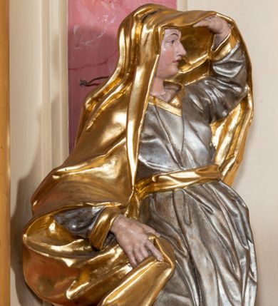 Zdjęcie nr 1: Figura drążona z tyłu, ustawiona na nieregularnej podstawie. Postać zwrócona w trzech czwartych w lewo, w kontrapoście, łukowato odchylona, lewą ręką unosi płaszcz nad głową, odsłaniając twarz, prawą przytrzymuje go na boku. Twarz ma pociągłą, z wyodrębnioną brodą, dużymi, głęboko osadzonymi, półprzymkniętymi oczami, zmarszczonymi brwiami, garbatym nosem i pełnymi, rozchylonymi ustami. Ubrana jest w srebrzoną, obfitą i silnie drapowaną suknię, ze złoconymi lamówkami, przepasaną złoconą szarfą. Na głowę i plecy ma narzucony obszerny, złocony płaszcz, opadający na prawy bok. Na stopach ma złocone sandały. Polichromia ciała naturalistyczna.