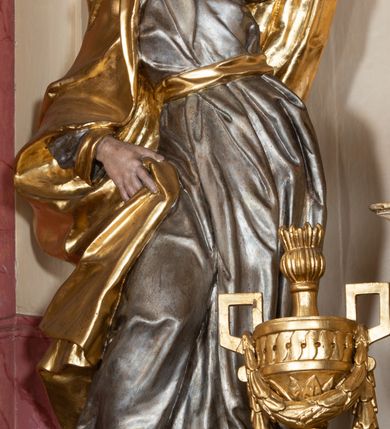 Zdjęcie nr 3: Figura drążona z tyłu, ustawiona na nieregularnej podstawie. Postać zwrócona w trzech czwartych w lewo, w kontrapoście, łukowato odchylona, lewą ręką unosi płaszcz nad głową, odsłaniając twarz, prawą przytrzymuje go na boku. Twarz ma pociągłą, z wyodrębnioną brodą, dużymi, głęboko osadzonymi, półprzymkniętymi oczami, zmarszczonymi brwiami, garbatym nosem i pełnymi, rozchylonymi ustami. Ubrana jest w srebrzoną, obfitą i silnie drapowaną suknię, ze złoconymi lamówkami, przepasaną złoconą szarfą. Na głowę i plecy ma narzucony obszerny, złocony płaszcz, opadający na prawy bok. Na stopach ma złocone sandały. Polichromia ciała naturalistyczna.