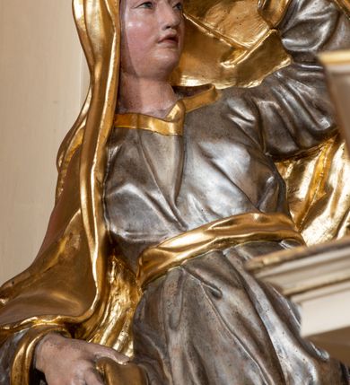 Zdjęcie nr 5: Figura drążona z tyłu, ustawiona na nieregularnej podstawie. Postać zwrócona w trzech czwartych w lewo, w kontrapoście, łukowato odchylona, lewą ręką unosi płaszcz nad głową, odsłaniając twarz, prawą przytrzymuje go na boku. Twarz ma pociągłą, z wyodrębnioną brodą, dużymi, głęboko osadzonymi, półprzymkniętymi oczami, zmarszczonymi brwiami, garbatym nosem i pełnymi, rozchylonymi ustami. Ubrana jest w srebrzoną, obfitą i silnie drapowaną suknię, ze złoconymi lamówkami, przepasaną złoconą szarfą. Na głowę i plecy ma narzucony obszerny, złocony płaszcz, opadający na prawy bok. Na stopach ma złocone sandały. Polichromia ciała naturalistyczna.