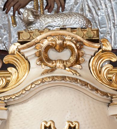 Zdjęcie nr 4: Tabernakulum w formie drewnianej, prostopadłościennej skrzynki, obitej blachą, z wypukłym frontem. Drzwiczki w kształcie stojącego prostokąta, w ramie, dekorowane przedstawieniem kielicha z hostią w glorii, ornamentem roślinnym i uskrzydloną główką anielską. Tron wystawienia ustawiony na dwustrefowym cokole, w którego partii zamontowane jest tabernakulum. Przyjmuje formę drewnianej, prostopadłościennej skrzynki z obrotową niszą, flankowaną dwiema parami kolumienek o kanelowanych trzonach, podtrzymujących fragmenty belkowania, nad niszą przyjmującego kształt falistego gzymsu, na którym znajduje się cokół dekorowany ornamentem roślinnym, z leżącym na księdze barankiem, flankowany dwoma aniołkami, Otwór niszy w formie stojącego prostokąta zamkniętego łukiem półkolistym zdobionym lambrekinem. Przed kolumienkami dwie figurki aniołów trzymających świeczniki.



