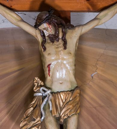 Zdjęcie nr 1: Grupę Ukrzyżowania, usytuowaną w obrębie ściany tęczowej, stanowi sylwetka Jezusa Ukrzyżowanego znajdująca się w górnej partii łuku tęczowego oraz dwie figury asystencyjne, Matki Boskiej i św. Jana Ewangelisty, u jego nasady. Przybitą trzema gwoźdźmi do drewnianego krzyża, pełnoplastyczną figurę Jezusa ukazano w typie Cristo morte. Zwrócona w prawo głowa wsparta jest na ramieniu. Pociągłą twarz charakteryzuje długi, prosty nos oraz krótki, ciemnobrązowy, dwudzielny zarost. Falowane pukle długich włosów opadają na plecy i klatkę piersiową. Ramiona ukształtowane są w głębokim zwisie w kształcie litery „U”. Sylwetkę Jezusa cechuje wydatna muskulatura ciała i sino-blady odcień karnacji. Anatomię torsu podkreśla wyrazista linia żeber. Biodra osłania przewiązane srebrzonym sznurem z prawej strony krótkie, złocone perizonium, z długim zwisem na prawym boku. Lekko ugięte w kolanach nogi przybite są jednym gwoździem. Głowę Jezusa wieńczy korona cierniowa, w prawym boku widoczna jest brocząca krwią rana. Na skroniach, nadgarstkach i stopach są drobne strugi krwi. W górnej partii krzyża biały titulus w formie zwoju, ze złoconym napisem „INRI”. Pod stopami Jezusa, u nasady krzyża jest para uskrzydlonych główek anielskich. Figury asystencyjne znajdują się u nasady łuku tęczowego, ustawione na prostopadłościennych cokołach. Charakteryzują je krępe proporcje sylwetek oraz sumaryczny modelunek fizjonomii i tkanin. Po prawej stronie znajduje się całopostaciowa figura św. Jana Ewangelisty spoglądającego ku górze, ubranego w srebrzoną suknię i jasnoczerwony płaszcz, z prawą ręką wyciągniętą w bok, lewą opuszczoną wzdłuż ciała. Po lewej jest całopostaciowa figura Matki Boskiej także spoglądającej ku górze, o rękach złożonych na piersiach. Ubrana jest w jasnoczerwoną suknię i błękitny, osłaniający głowę płaszcz. 