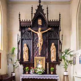 Zdjęcie nr 1: Ołtarz przyścienny, architektoniczny, jednokondygnacyjny. Ołtarz jest prostopadłościenny, z drewnianą mensą. Trójosiowe, artykułowane smukłymi filarkami retabulum osadzone jest na predelli zdobionej fryzem arkadkowym zamknięte rodzajem fryzu przerwanego pośrodku ostrołukową wimpergą. Pole środkowej osi nastawy zajmuje płycina w kształcie stojącego prostokąta zamkniętego półkolistym łukiem nadwieszonym, wypełniona płaskorzeźbionym motywem czwórliści. Wyżej znajduje się dekoracja maswerkowa częściowo wpisana  w okrąg. Osie boczne mają formę płytkich, ostrołukowych wnęk zdobionych motywem kwietnych gałązek wpisanych w romboidalne pola. Partie łuków wypełnia ażurowy ornament astwerkowy. Retabulum ujmuje po bokach para uszaków w formie ażurowych przypór zwieńczonych pinaklami. Fryz zamykający retabulum wieńczy para wyższych pośrodku i niższych po bokach pinakli, natomiast wimpergę niewielki kwiaton. W osi środkowej znajduje się figura Jezusa Ukrzyżowanego, w prawej figura św. Jana Ewangelisty, w lewej Matki Boskiej Bolesnej. 

Struktura ołtarza pokryta jest ciemnobrązową bejcą, figury utrzymane są w odcieniu naturalnego drewna.

