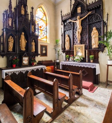 Zdjęcie nr 5: Ołtarz przyścienny, architektoniczny, jednokondygnacyjny. Ołtarz jest prostopadłościenny, z drewnianą mensą. Trójosiowe, artykułowane smukłymi filarkami retabulum osadzone jest na predelli zdobionej fryzem arkadkowym zamknięte rodzajem fryzu przerwanego pośrodku ostrołukową wimpergą. Pole środkowej osi nastawy zajmuje płycina w kształcie stojącego prostokąta zamkniętego półkolistym łukiem nadwieszonym, wypełniona płaskorzeźbionym motywem czwórliści. Wyżej znajduje się dekoracja maswerkowa częściowo wpisana  w okrąg. Osie boczne mają formę płytkich, ostrołukowych wnęk zdobionych motywem kwietnych gałązek wpisanych w romboidalne pola. Partie łuków wypełnia ażurowy ornament astwerkowy. Retabulum ujmuje po bokach para uszaków w formie ażurowych przypór zwieńczonych pinaklami. Fryz zamykający retabulum wieńczy para wyższych pośrodku i niższych po bokach pinakli, natomiast wimpergę niewielki kwiaton. W osi środkowej znajduje się figura Jezusa Ukrzyżowanego, w prawej figura św. Jana Ewangelisty, w lewej Matki Boskiej Bolesnej. 

Struktura ołtarza pokryta jest ciemnobrązową bejcą, figury utrzymane są w odcieniu naturalnego drewna.

