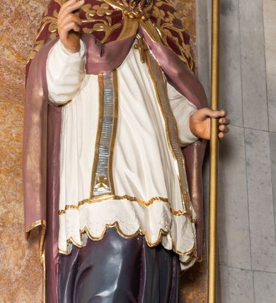 Zdjęcie nr 2: Rzeźba drążona z tyłu stoi na prostokątnej podstawie ustawionej na profilowanej, zwężającej się ku dołowi konsoli przyściennej. Postać biskupa jest ujęta frontalni w nieznacznym kontrapoście z głową lekko skierowaną w prawo. Prawą rękę Marcin ma uniesioną przed siebie na wysokość piersi w lewej zaś trzyma laskę krzyżową. Święty ma pociągłą, wychudzoną twarz o szeroko otwartych oczach, mięsistym nosie i pełnych ustach. Głowę okala broda i lekko kręcone sięgające ramion włosy. Marcin na głowie ma szkarłatną mitrę zdobiną złotą ornamentyką. Ubrany jest w sutannę, białą komże dekorowaną u spodu szeroką koronką, stułę oraz szkarłatną kapę pokrytą złocistym ornamentem i lamowaną złotą tasiemką. Na postumencie widoczny jest podpis: &quot;Ś[WIĘTY] MARCIN&quot;.