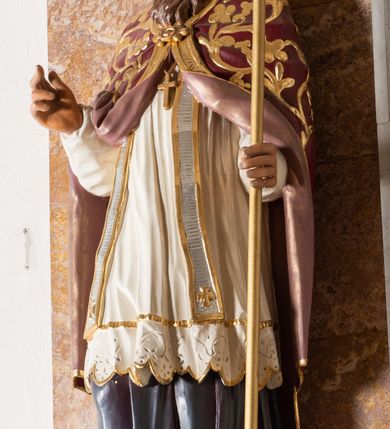 Zdjęcie nr 3: Rzeźba drążona z tyłu stoi na prostokątnej podstawie ustawionej na profilowanej, zwężającej się ku dołowi konsoli przyściennej. Postać biskupa jest ujęta frontalni w nieznacznym kontrapoście z głową lekko skierowaną w prawo. Prawą rękę Marcin ma uniesioną przed siebie na wysokość piersi w lewej zaś trzyma laskę krzyżową. Święty ma pociągłą, wychudzoną twarz o szeroko otwartych oczach, mięsistym nosie i pełnych ustach. Głowę okala broda i lekko kręcone sięgające ramion włosy. Marcin na głowie ma szkarłatną mitrę zdobiną złotą ornamentyką. Ubrany jest w sutannę, białą komże dekorowaną u spodu szeroką koronką, stułę oraz szkarłatną kapę pokrytą złocistym ornamentem i lamowaną złotą tasiemką. Na postumencie widoczny jest podpis: "Ś[WIĘTY] MARCIN".