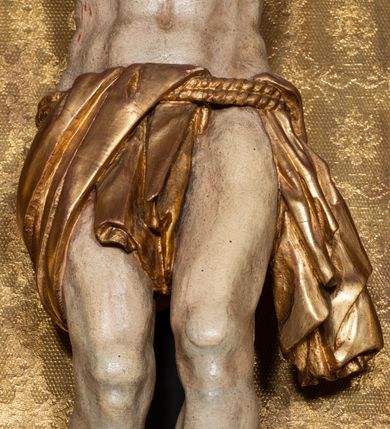 Zdjęcie nr 17: Na dużym krzyżu z ciemnego drewna zawieszono polichromowaną figurę martwego Chrystusa o szeroko rozpostartych ramionach. Ciało Zbawiciela do krzyża jest przymocowane za pomocą trzech gwoździ. On sam został ukazany jako martwy z zamkniętymi oczami i nieznacznie słaniającą się głową. Jego postać jest wysmuklona z realistycznie potraktowaną muskulaturą korpusu. Wyraźnie zaznaczono naprężone ścięgna i mięśnie na całym ciele, co ma sprawiać wrażenie jego autentyczności. Mocno również zaznaczono krwawiącą wybroczynę z przebitego prawego boku. Ciało jest wychudzone o zapadłej klatce piersiowej z silnie podkreśloną linią żeber i mostkiem. Prawa stopa założona jest na lewą. Twarz Zbawiciel jest pociągłą z wyrazistym nosem i wąskim, nieznacznie rozchylonymi ustami. Głowę otaczają brązowe włosy spływające puklami na oba ramiona oraz brązowa broda. Chrystus ma na głowie złoconą, cierniową koronę z długimi cierniami, spod której na czoło spływają krople krwi. Biodra Zbawiciela przepasane są złoconym, krótkim perizonium w formie chusty przerzuconej przez podwójny sznur, odsłaniającej lewe udo i układające się w feston z prawej strony. Ponad głową Chrystusa na pionowej belce krzyża zawieszono rozwiany titulus z napisem "IN / RI".