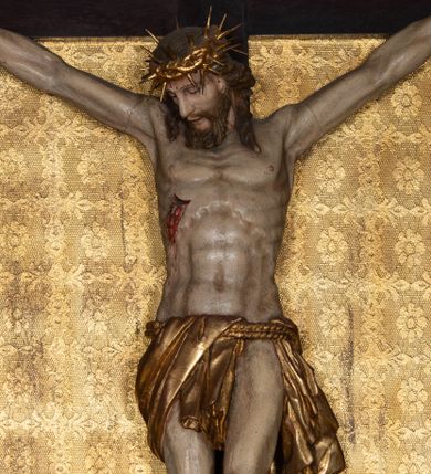 Zdjęcie nr 1: Na dużym krzyżu z ciemnego drewna zawieszono polichromowaną figurę martwego Chrystusa o szeroko rozpostartych ramionach. Ciało Zbawiciela do krzyża jest przymocowane za pomocą trzech gwoździ. On sam został ukazany jako martwy z zamkniętymi oczami i nieznacznie słaniającą się głową. Jego postać jest wysmuklona z realistycznie potraktowaną muskulaturą korpusu. Wyraźnie zaznaczono naprężone ścięgna i mięśnie na całym ciele, co ma sprawiać wrażenie jego autentyczności. Mocno również zaznaczono krwawiącą wybroczynę z przebitego prawego boku. Ciało jest wychudzone o zapadłej klatce piersiowej z silnie podkreśloną linią żeber i mostkiem. Prawa stopa założona jest na lewą. Twarz Zbawiciel jest pociągłą z wyrazistym nosem i wąskim, nieznacznie rozchylonymi ustami. Głowę otaczają brązowe włosy spływające puklami na oba ramiona oraz brązowa broda. Chrystus ma na głowie złoconą, cierniową koronę z długimi cierniami, spod której na czoło spływają krople krwi. Biodra Zbawiciela przepasane są złoconym, krótkim perizonium w formie chusty przerzuconej przez podwójny sznur, odsłaniającej lewe udo i układające się w feston z prawej strony. Ponad głową Chrystusa na pionowej belce krzyża zawieszono rozwiany titulus z napisem "IN / RI".
