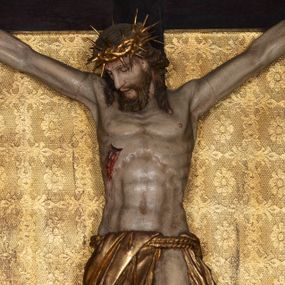 Zdjęcie nr 1: Na dużym krzyżu z ciemnego drewna zawieszono polichromowaną figurę martwego Chrystusa o szeroko rozpostartych ramionach. Ciało Zbawiciela do krzyża jest przymocowane za pomocą trzech gwoździ. On sam został ukazany jako martwy z zamkniętymi oczami i nieznacznie słaniającą się głową. Jego postać jest wysmuklona z realistycznie potraktowaną muskulaturą korpusu. Wyraźnie zaznaczono naprężone ścięgna i mięśnie na całym ciele, co ma sprawiać wrażenie jego autentyczności. Mocno również zaznaczono krwawiącą wybroczynę z przebitego prawego boku. Ciało jest wychudzone o zapadłej klatce piersiowej z silnie podkreśloną linią żeber i mostkiem. Prawa stopa założona jest na lewą. Twarz Zbawiciel jest pociągłą z wyrazistym nosem i wąskim, nieznacznie rozchylonymi ustami. Głowę otaczają brązowe włosy spływające puklami na oba ramiona oraz brązowa broda. Chrystus ma na głowie złoconą, cierniową koronę z długimi cierniami, spod której na czoło spływają krople krwi. Biodra Zbawiciela przepasane są złoconym, krótkim perizonium w formie chusty przerzuconej przez podwójny sznur, odsłaniającej lewe udo i układające się w feston z prawej strony. Ponad głową Chrystusa na pionowej belce krzyża zawieszono rozwiany titulus z napisem &quot;IN / RI&quot;.