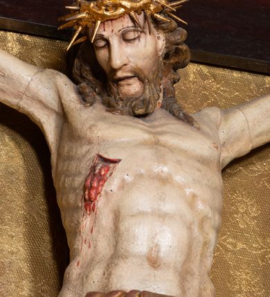 Zdjęcie nr 2: Na dużym krzyżu z ciemnego drewna zawieszono polichromowaną figurę martwego Chrystusa o szeroko rozpostartych ramionach. Ciało Zbawiciela do krzyża jest przymocowane za pomocą trzech gwoździ. On sam został ukazany jako martwy z zamkniętymi oczami i nieznacznie słaniającą się głową. Jego postać jest wysmuklona z realistycznie potraktowaną muskulaturą korpusu. Wyraźnie zaznaczono naprężone ścięgna i mięśnie na całym ciele, co ma sprawiać wrażenie jego autentyczności. Mocno również zaznaczono krwawiącą wybroczynę z przebitego prawego boku. Ciało jest wychudzone o zapadłej klatce piersiowej z silnie podkreśloną linią żeber i mostkiem. Prawa stopa założona jest na lewą. Twarz Zbawiciel jest pociągłą z wyrazistym nosem i wąskim, nieznacznie rozchylonymi ustami. Głowę otaczają brązowe włosy spływające puklami na oba ramiona oraz brązowa broda. Chrystus ma na głowie złoconą, cierniową koronę z długimi cierniami, spod której na czoło spływają krople krwi. Biodra Zbawiciela przepasane są złoconym, krótkim perizonium w formie chusty przerzuconej przez podwójny sznur, odsłaniającej lewe udo i układające się w feston z prawej strony. Ponad głową Chrystusa na pionowej belce krzyża zawieszono rozwiany titulus z napisem "IN / RI".