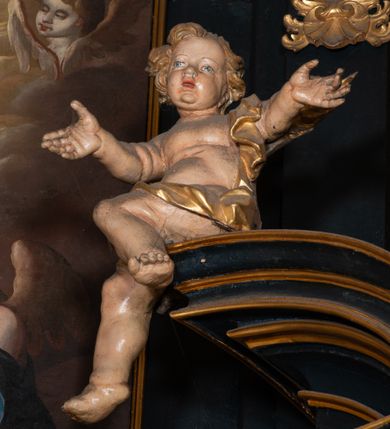 Zdjęcie nr 7: Na dużym krzyżu z ciemnego drewna zawieszono polichromowaną figurę martwego Chrystusa o szeroko rozpostartych ramionach. Ciało Zbawiciela do krzyża jest przymocowane za pomocą trzech gwoździ. On sam został ukazany jako martwy z zamkniętymi oczami i nieznacznie słaniającą się głową. Jego postać jest wysmuklona z realistycznie potraktowaną muskulaturą korpusu. Wyraźnie zaznaczono naprężone ścięgna i mięśnie na całym ciele, co ma sprawiać wrażenie jego autentyczności. Mocno również zaznaczono krwawiącą wybroczynę z przebitego prawego boku. Ciało jest wychudzone o zapadłej klatce piersiowej z silnie podkreśloną linią żeber i mostkiem. Prawa stopa założona jest na lewą. Twarz Zbawiciel jest pociągłą z wyrazistym nosem i wąskim, nieznacznie rozchylonymi ustami. Głowę otaczają brązowe włosy spływające puklami na oba ramiona oraz brązowa broda. Chrystus ma na głowie złoconą, cierniową koronę z długimi cierniami, spod której na czoło spływają krople krwi. Biodra Zbawiciela przepasane są złoconym, krótkim perizonium w formie chusty przerzuconej przez podwójny sznur, odsłaniającej lewe udo i układające się w feston z prawej strony. Ponad głową Chrystusa na pionowej belce krzyża zawieszono rozwiany titulus z napisem &quot;IN / RI&quot;.