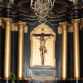 Zdjęcie nr 1: Ołtarz boczny przyjął formę przyściennej, jednokondygnacyjnej i jednoosiowej struktury architektonicznej ze zwieńczeniem. Drewniany stipes ołtarzowy w formie sarkofagu na cokole ustawiono na trójstopniowym podeście. Całą nastawę ustawiono na wysokim, dwustrefowym postumencie, na którym wsparto niski cokół, podtrzymujący zwielokrotnione pilastry o gładkich trzonach i głowicach korynckich oraz flankujący kondygnację dwie pary kolumn. Podpory wspierają wklęsło-wypuklę belkowanie wyłamane na osi kolumn, z umieszczonym na nim na osi pola obrazowego fantazyjnym kartuszem z przedstawieniem gołębicy jako Ducha Świętego. Na belkowaniu, na osi kolumn skrajnych, usytuowano rzeźby stojących aniołów, a na osi kolumn środkowych elementy półkolistego, przerwanego przyczółku z siedzącymi dwoma aniołkami. Zwieńczenie uzyskało kształt leżącego prostokąta o wklęsłych bokach, przechodzących w spływy wolutowe z pilastrami flankującymi pole obrazowe, podtrzymujące wyłamany na osi pilastrów i nadwieszone nad polem obrazowym profilowany gzyms koronujący. Na osi pilastrów ustawiono na nim dwa przyczółki faliste, a na osi retabulum promienistą glorię z chrystogramem "IHS" otoczonym obłokami. Pole obrazowe w kondygnacji uzyskało kształt stojącego prostokąta ujętego profilowaną ramą o nieznacznie wklęsłych bokach i podstawie, zwieńczonego łukiem nadwieszonym z uskokiem. W nim na złoconym tle zawieszono drewniany krucyfiks. Poniżej pola widoczna jest podłużna, prostokątna płycina. W polu zwieńczenia w kształcie obramionego profilem stojącego prostokąta zamkniętego nadwieszonym łukiem odcinkowym zainstalowano obraz z okiem Bożej Opatrzności. Całość retabulum polichromowano na czarno, natomiast kolumny, głowice pilastrów, profile o szaty aniołów i ich skrzydła wyzłocono. Rzeźby aniołów uzyskały polichromię naturalistyczną.    