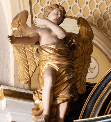 Zdjęcie nr 10: Ołtarz boczny przyjął formę przyściennej, jednokondygnacyjnej i jednoosiowej struktury architektonicznej ze zwieńczeniem. Drewniany stipes ołtarzowy w formie sarkofagu na cokole ustawiono na trójstopniowym podeście. Całą nastawę ustawiono na wysokim, dwustrefowym postumencie, na którym wsparto niski cokół, podtrzymujący zwielokrotnione pilastry o gładkich trzonach i głowicach korynckich oraz flankujący kondygnację dwie pary kolumn. Podpory wspierają wklęsło-wypuklę belkowanie wyłamane na osi kolumn, z umieszczonym na nim na osi pola obrazowego fantazyjnym kartuszem z przedstawieniem gołębicy jako Ducha Świętego. Na belkowaniu, na osi kolumn skrajnych, usytuowano rzeźby stojących aniołów, a na osi kolumn środkowych elementy półkolistego, przerwanego przyczółku z siedzącymi dwoma aniołkami. Zwieńczenie uzyskało kształt leżącego prostokąta o wklęsłych bokach, przechodzących w spływy wolutowe z pilastrami flankującymi pole obrazowe, podtrzymujące wyłamany na osi pilastrów i nadwieszone nad polem obrazowym profilowany gzyms koronujący. Na osi pilastrów ustawiono na nim dwa przyczółki faliste, a na osi retabulum promienistą glorię z chrystogramem "IHS" otoczonym obłokami. Pole obrazowe w kondygnacji uzyskało kształt stojącego prostokąta ujętego profilowaną ramą o nieznacznie wklęsłych bokach i podstawie, zwieńczonego łukiem nadwieszonym z uskokiem. W nim na złoconym tle zawieszono drewniany krucyfiks. Poniżej pola widoczna jest podłużna, prostokątna płycina. W polu zwieńczenia w kształcie obramionego profilem stojącego prostokąta zamkniętego nadwieszonym łukiem odcinkowym zainstalowano obraz z okiem Bożej Opatrzności. Całość retabulum polichromowano na czarno, natomiast kolumny, głowice pilastrów, profile o szaty aniołów i ich skrzydła wyzłocono. Rzeźby aniołów uzyskały polichromię naturalistyczną.    