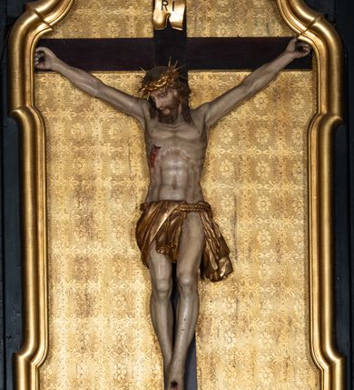 Zdjęcie nr 13: Ołtarz boczny przyjął formę przyściennej, jednokondygnacyjnej i jednoosiowej struktury architektonicznej ze zwieńczeniem. Drewniany stipes ołtarzowy w formie sarkofagu na cokole ustawiono na trójstopniowym podeście. Całą nastawę ustawiono na wysokim, dwustrefowym postumencie, na którym wsparto niski cokół, podtrzymujący zwielokrotnione pilastry o gładkich trzonach i głowicach korynckich oraz flankujący kondygnację dwie pary kolumn. Podpory wspierają wklęsło-wypuklę belkowanie wyłamane na osi kolumn, z umieszczonym na nim na osi pola obrazowego fantazyjnym kartuszem z przedstawieniem gołębicy jako Ducha Świętego. Na belkowaniu, na osi kolumn skrajnych, usytuowano rzeźby stojących aniołów, a na osi kolumn środkowych elementy półkolistego, przerwanego przyczółku z siedzącymi dwoma aniołkami. Zwieńczenie uzyskało kształt leżącego prostokąta o wklęsłych bokach, przechodzących w spływy wolutowe z pilastrami flankującymi pole obrazowe, podtrzymujące wyłamany na osi pilastrów i nadwieszone nad polem obrazowym profilowany gzyms koronujący. Na osi pilastrów ustawiono na nim dwa przyczółki faliste, a na osi retabulum promienistą glorię z chrystogramem &quot;IHS&quot; otoczonym obłokami. Pole obrazowe w kondygnacji uzyskało kształt stojącego prostokąta ujętego profilowaną ramą o nieznacznie wklęsłych bokach i podstawie, zwieńczonego łukiem nadwieszonym z uskokiem. W nim na złoconym tle zawieszono drewniany krucyfiks. Poniżej pola widoczna jest podłużna, prostokątna płycina. W polu zwieńczenia w kształcie obramionego profilem stojącego prostokąta zamkniętego nadwieszonym łukiem odcinkowym zainstalowano obraz z okiem Bożej Opatrzności. Całość retabulum polichromowano na czarno, natomiast kolumny, głowice pilastrów, profile o szaty aniołów i ich skrzydła wyzłocono. Rzeźby aniołów uzyskały polichromię naturalistyczną.    