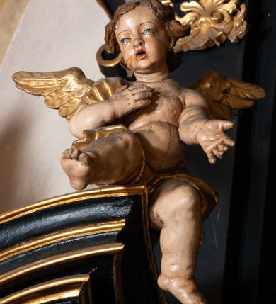 Zdjęcie nr 7: Ołtarz boczny przyjął formę przyściennej, jednokondygnacyjnej i jednoosiowej struktury architektonicznej ze zwieńczeniem. Drewniany stipes ołtarzowy w formie sarkofagu na cokole ustawiono na trójstopniowym podeście. Całą nastawę ustawiono na wysokim, dwustrefowym postumencie, na którym wsparto niski cokół, podtrzymujący zwielokrotnione pilastry o gładkich trzonach i głowicach korynckich oraz flankujący kondygnację dwie pary kolumn. Podpory wspierają wklęsło-wypuklę belkowanie wyłamane na osi kolumn, z umieszczonym na nim na osi pola obrazowego fantazyjnym kartuszem z przedstawieniem gołębicy jako Ducha Świętego. Na belkowaniu, na osi kolumn skrajnych, usytuowano rzeźby stojących aniołów, a na osi kolumn środkowych elementy półkolistego, przerwanego przyczółku z siedzącymi dwoma aniołkami. Zwieńczenie uzyskało kształt leżącego prostokąta o wklęsłych bokach, przechodzących w spływy wolutowe z pilastrami flankującymi pole obrazowe, podtrzymujące wyłamany na osi pilastrów i nadwieszone nad polem obrazowym profilowany gzyms koronujący. Na osi pilastrów ustawiono na nim dwa przyczółki faliste, a na osi retabulum promienistą glorię z chrystogramem "IHS" otoczonym obłokami. Pole obrazowe w kondygnacji uzyskało kształt stojącego prostokąta ujętego profilowaną ramą o nieznacznie wklęsłych bokach i podstawie, zwieńczonego łukiem nadwieszonym z uskokiem. W nim na złoconym tle zawieszono drewniany krucyfiks. Poniżej pola widoczna jest podłużna, prostokątna płycina. W polu zwieńczenia w kształcie obramionego profilem stojącego prostokąta zamkniętego nadwieszonym łukiem odcinkowym zainstalowano obraz z okiem Bożej Opatrzności. Całość retabulum polichromowano na czarno, natomiast kolumny, głowice pilastrów, profile o szaty aniołów i ich skrzydła wyzłocono. Rzeźby aniołów uzyskały polichromię naturalistyczną.    