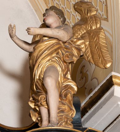 Zdjęcie nr 14: Ołtarz boczny przyjął formę przyściennej, jednokondygnacyjnej i jednoosiowej struktury architektonicznej ze zwieńczeniem. Drewniany stipes ołtarzowy w formie sarkofagu na cokole ustawiono na trójstopniowym podeście. Całą nastawę ustawiono na wysokim, dwustrefowym postumencie, na którym wsparto niski cokół, podtrzymujący zwielokrotnione pilastry o gładkich trzonach i głowicach korynckich oraz flankujący kondygnację dwie pary kolumn. Podpory wspierają wklęsło-wypuklę belkowanie wyłamane na osi kolumn, z umieszczonym na nim na osi pola obrazowego fantazyjnym kartuszem z przedstawieniem gołębicy jako Ducha Świętego. Na belkowaniu, na osi kolumn skrajnych, usytuowano rzeźby stojących aniołów, a na osi kolumn środkowych elementy półkolistego, przerwanego przyczółku z siedzącymi dwoma aniołkami. Zwieńczenie uzyskało kształt leżącego prostokąta o wklęsłych bokach, przechodzących w spływy wolutowe z pilastrami flankującymi pole obrazowe, podtrzymujące wyłamany na osi pilastrów i nadwieszone nad polem obrazowym profilowany gzyms koronujący. Na osi pilastrów ustawiono na nim dwa przyczółki faliste, a na osi retabulum promienistą glorię z chrystogramem "IHS" otoczonym obłokami. Pole obrazowe w kondygnacji uzyskało kształt stojącego prostokąta ujętego profilowaną ramą o nieznacznie wklęsłych bokach i podstawie, zwieńczonego łukiem nadwieszonym z uskokiem. W nim na złoconym tle zawieszono drewniany krucyfiks. Poniżej pola widoczna jest podłużna, prostokątna płycina. W polu zwieńczenia w kształcie obramionego profilem stojącego prostokąta zamkniętego nadwieszonym łukiem odcinkowym zainstalowano obraz z okiem Bożej Opatrzności. Całość retabulum polichromowano na czarno, natomiast kolumny, głowice pilastrów, profile o szaty aniołów i ich skrzydła wyzłocono. Rzeźby aniołów uzyskały polichromię naturalistyczną.    