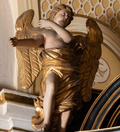Zdjęcie nr 11: Ołtarz boczny przyjął formę przyściennej, jednokondygnacyjnej i jednoosiowej struktury architektonicznej ze zwieńczeniem. Drewniany stipes ołtarzowy w formie sarkofagu na cokole ustawiono na trójstopniowym podeście. Całą nastawę ustawiono na wysokim, dwustrefowym postumencie, na którym wsparto niski cokół, podtrzymujący zwielokrotnione pilastry o gładkich trzonach i głowicach korynckich oraz flankujący kondygnację dwie pary kolumn. Podpory wspierają wklęsło-wypuklę belkowanie wyłamane na osi kolumn, z umieszczonym na nim na osi pola obrazowego fantazyjnym kartuszem z przedstawieniem gołębicy jako Ducha Świętego. Na belkowaniu, na osi kolumn skrajnych, usytuowano rzeźby stojących aniołów, a na osi kolumn środkowych elementy półkolistego, przerwanego przyczółku z siedzącymi dwoma aniołkami. Zwieńczenie uzyskało kształt leżącego prostokąta o wklęsłych bokach, przechodzących w spływy wolutowe z pilastrami flankującymi pole obrazowe, podtrzymujące wyłamany na osi pilastrów i nadwieszone nad polem obrazowym profilowany gzyms koronujący. Na osi pilastrów ustawiono na nim dwa przyczółki faliste, a na osi retabulum promienistą glorię z chrystogramem "IHS" otoczonym obłokami. Pole obrazowe w kondygnacji uzyskało kształt stojącego prostokąta ujętego profilowaną ramą o nieznacznie wklęsłych bokach i podstawie, zwieńczonego łukiem nadwieszonym z uskokiem. W nim na złoconym tle zawieszono drewniany krucyfiks. Poniżej pola widoczna jest podłużna, prostokątna płycina. W polu zwieńczenia w kształcie obramionego profilem stojącego prostokąta zamkniętego nadwieszonym łukiem odcinkowym zainstalowano obraz z okiem Bożej Opatrzności. Całość retabulum polichromowano na czarno, natomiast kolumny, głowice pilastrów, profile o szaty aniołów i ich skrzydła wyzłocono. Rzeźby aniołów uzyskały polichromię naturalistyczną.    