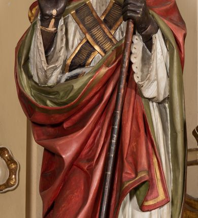 Zdjęcie nr 7: Nastawa ołtarzowa uzyskała charakter jednoosiowej, jednokondygnacyjnej przestrzennej struktury architektonicznej ze zwieńczeniem. Drewniany stipes ołtarzowy przyjął kształt zwężającego się ku dołowi sarkofagu wspierającego mensę, ustawionego na marmurowym podeście o dwu stopniach. Na mensie na osi ustawiono prostopadłościenne tabernakulum na rzucie trapezu, ujęte po bokach spływami wolutowym podtrzymującymi proste belkowanie wyłamane na osi podpór. Drzwiczki do tabernakulum uzyskały kształt stojącego prostokąta zamkniętego u góry łukiem nadwieszonym z uskokiem. W ich polu ukazano kielich z hostią. Retabulum wykonano na rzucie dwóch koncentrycznych półkoli. Pierwsze, tworzy przyścienna struktura flankowana dwoma esowatymi splotami wolutowymi podtrzymującymi architraw z belkowaniem zdobionym fryzem kostkowym, podtrzymującym w osiach skrajnych dwa wolutowe postumenty przechodzące w zwieńczenie. Zwieńczenie utworzono z płyciny w kształcie leżącego prostokąta o wklęsłych bokach zwieńczone gzymsem koronującym wygiętym w formie nadwieszonego łuku odcinkowego. W polu zwieńczenia umieszczono płaskorzeźbiony kartusz z monogramem maryjnym w czerwonym polu flankowany przez dwa uskrzydlone aniołki. Drugie półkole uzyskano z wysunięcia przed lico nastawy dwóch kolumn wspartych na wysokich, dwupoziomowych postumentach oraz flankujących główne pole obrazowe kondygnacji dwóch pilastrów podtrzymujących półkoliście wygięty architraw z belkowaniem, na końcach którego umieszczono przerwane wolutowe przyczółki faliste z siedzącymi na nich dwoma aniołami podtrzymującymi zawieszoną na osi monumentalną koronę zamknietą. Kolumny i pilastry o korynckich kapitelach i głowicach w dwóch trzecich od góry są kanelowane, a niżej gładkie i zdobione wstęgami z zawieszonymi zwisami owocowymi. Podtrzymujące kolumny postumenty ozdobiono niebieskimi, prostokątnymi płycinami u góry zamkniętymi półkoliście, a u dołu wklęsłymi. Po osiach zewnętrznych do postumentów przylegają konsole zdobione akantowymi wolutami, na których ustawiono figury św. Wojciech i św. Stanisława. Architraw drugiego półkola ozdobiono rytmiczne rozmieszczonymi partiami ornamentu roślinnego, a belkowanie i przyczółki faliste fryzem kostkowym. W polu kondygnacji umieszczono pole obrazowe w formie stojącego prostokąta zamkniętego od góry łukiem odcinkowym nadwieszonym obramienionym ramą zdobioną ażurową wicią akantową. W polu znajduje się obraz Matki Boskiej z Dzieciątkiem w rzymskim typie Salus Populi Romani, a na zasuwie obraz przedstawiający wybór św. Macieja na apostoła. Strukturę ołtarza pomalowano w tonacji ciemnej kości słoniowej. Kolumny, profile oraz ornamenty zostały wyzłocone. Rzeźby św. Wojciech i św. Stanisława uzyskały naturalistyczną polichromię podobnie jak anioły podtrzymujące koronę.  