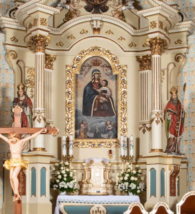 Zdjęcie nr 1: Nastawa ołtarzowa uzyskała charakter jednoosiowej, jednokondygnacyjnej przestrzennej struktury architektonicznej ze zwieńczeniem. Drewniany stipes ołtarzowy przyjął kształt zwężającego się ku dołowi sarkofagu wspierającego mensę, ustawionego na marmurowym podeście o dwu stopniach. Na mensie na osi ustawiono prostopadłościenne tabernakulum na rzucie trapezu, ujęte po bokach spływami wolutowym podtrzymującymi proste belkowanie wyłamane na osi podpór. Drzwiczki do tabernakulum uzyskały kształt stojącego prostokąta zamkniętego u góry łukiem nadwieszonym z uskokiem. W ich polu ukazano kielich z hostią. Retabulum wykonano na rzucie dwóch koncentrycznych półkoli. Pierwsze, tworzy przyścienna struktura flankowana dwoma esowatymi splotami wolutowymi podtrzymującymi architraw z belkowaniem zdobionym fryzem kostkowym, podtrzymującym w osiach skrajnych dwa wolutowe postumenty przechodzące w zwieńczenie. Zwieńczenie utworzono z płyciny w kształcie leżącego prostokąta o wklęsłych bokach zwieńczone gzymsem koronującym wygiętym w formie nadwieszonego łuku odcinkowego. W polu zwieńczenia umieszczono płaskorzeźbiony kartusz z monogramem maryjnym w czerwonym polu flankowany przez dwa uskrzydlone aniołki. Drugie półkole uzyskano z wysunięcia przed lico nastawy dwóch kolumn wspartych na wysokich, dwupoziomowych postumentach oraz flankujących główne pole obrazowe kondygnacji dwóch pilastrów podtrzymujących półkoliście wygięty architraw z belkowaniem, na końcach którego umieszczono przerwane wolutowe przyczółki faliste z siedzącymi na nich dwoma aniołami podtrzymującymi zawieszoną na osi monumentalną koronę zamknietą. Kolumny i pilastry o korynckich kapitelach i głowicach w dwóch trzecich od góry są kanelowane, a niżej gładkie i zdobione wstęgami z zawieszonymi zwisami owocowymi. Podtrzymujące kolumny postumenty ozdobiono niebieskimi, prostokątnymi płycinami u góry zamkniętymi półkoliście, a u dołu wklęsłymi. Po osiach zewnętrznych do postumentów przylegają konsole zdobione akantowymi wolutami, na których ustawiono figury św. Wojciech i św. Stanisława. Architraw drugiego półkola ozdobiono rytmiczne rozmieszczonymi partiami ornamentu roślinnego, a belkowanie i przyczółki faliste fryzem kostkowym. W polu kondygnacji umieszczono pole obrazowe w formie stojącego prostokąta zamkniętego od góry łukiem odcinkowym nadwieszonym obramienionym ramą zdobioną ażurową wicią akantową. W polu znajduje się obraz Matki Boskiej z Dzieciątkiem w rzymskim typie Salus Populi Romani, a na zasuwie obraz przedstawiający wybór św. Macieja na apostoła. Strukturę ołtarza pomalowano w tonacji ciemnej kości słoniowej. Kolumny, profile oraz ornamenty zostały wyzłocone. Rzeźby św. Wojciech i św. Stanisława uzyskały naturalistyczną polichromię podobnie jak anioły podtrzymujące koronę.  