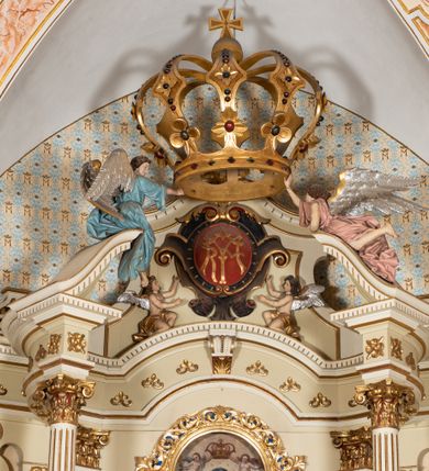 Zdjęcie nr 11: Nastawa ołtarzowa uzyskała charakter jednoosiowej, jednokondygnacyjnej przestrzennej struktury architektonicznej ze zwieńczeniem. Drewniany stipes ołtarzowy przyjął kształt zwężającego się ku dołowi sarkofagu wspierającego mensę, ustawionego na marmurowym podeście o dwu stopniach. Na mensie na osi ustawiono prostopadłościenne tabernakulum na rzucie trapezu, ujęte po bokach spływami wolutowym podtrzymującymi proste belkowanie wyłamane na osi podpór. Drzwiczki do tabernakulum uzyskały kształt stojącego prostokąta zamkniętego u góry łukiem nadwieszonym z uskokiem. W ich polu ukazano kielich z hostią. Retabulum wykonano na rzucie dwóch koncentrycznych półkoli. Pierwsze, tworzy przyścienna struktura flankowana dwoma esowatymi splotami wolutowymi podtrzymującymi architraw z belkowaniem zdobionym fryzem kostkowym, podtrzymującym w osiach skrajnych dwa wolutowe postumenty przechodzące w zwieńczenie. Zwieńczenie utworzono z płyciny w kształcie leżącego prostokąta o wklęsłych bokach zwieńczone gzymsem koronującym wygiętym w formie nadwieszonego łuku odcinkowego. W polu zwieńczenia umieszczono płaskorzeźbiony kartusz z monogramem maryjnym w czerwonym polu flankowany przez dwa uskrzydlone aniołki. Drugie półkole uzyskano z wysunięcia przed lico nastawy dwóch kolumn wspartych na wysokich, dwupoziomowych postumentach oraz flankujących główne pole obrazowe kondygnacji dwóch pilastrów podtrzymujących półkoliście wygięty architraw z belkowaniem, na końcach którego umieszczono przerwane wolutowe przyczółki faliste z siedzącymi na nich dwoma aniołami podtrzymującymi zawieszoną na osi monumentalną koronę zamknietą. Kolumny i pilastry o korynckich kapitelach i głowicach w dwóch trzecich od góry są kanelowane, a niżej gładkie i zdobione wstęgami z zawieszonymi zwisami owocowymi. Podtrzymujące kolumny postumenty ozdobiono niebieskimi, prostokątnymi płycinami u góry zamkniętymi półkoliście, a u dołu wklęsłymi. Po osiach zewnętrznych do postumentów przylegają konsole zdobione akantowymi wolutami, na których ustawiono figury św. Wojciech i św. Stanisława. Architraw drugiego półkola ozdobiono rytmiczne rozmieszczonymi partiami ornamentu roślinnego, a belkowanie i przyczółki faliste fryzem kostkowym. W polu kondygnacji umieszczono pole obrazowe w formie stojącego prostokąta zamkniętego od góry łukiem odcinkowym nadwieszonym obramienionym ramą zdobioną ażurową wicią akantową. W polu znajduje się obraz Matki Boskiej z Dzieciątkiem w rzymskim typie Salus Populi Romani, a na zasuwie obraz przedstawiający wybór św. Macieja na apostoła. Strukturę ołtarza pomalowano w tonacji ciemnej kości słoniowej. Kolumny, profile oraz ornamenty zostały wyzłocone. Rzeźby św. Wojciech i św. Stanisława uzyskały naturalistyczną polichromię podobnie jak anioły podtrzymujące koronę.  