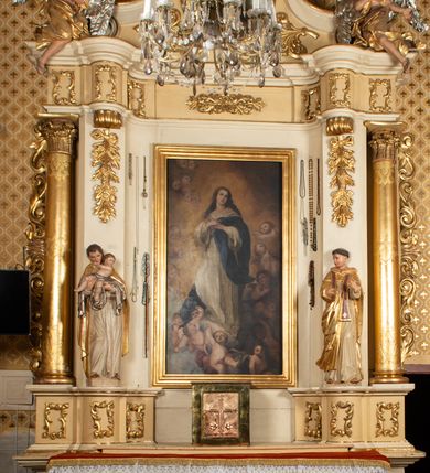 Zdjęcie nr 2: Nastawa ołtarzowa uzyskała charakter przyściennego retabulum jednoosiowego, jednokondygnacyjnego ze zwieńczeniem. Drewniany stipes ołtarzowy przyjął kształt zwężającego się ku dołowi sarkofagu ustawionego na jednostopniowym podeście. Na mensie na osi ustawiono prostopadłościenne tabernakulum obite blachą w formie skrzynki. Drzwiczki do tabernakulum ozdobiono puncowanym krzyżem. Kondygnację nastawy ujmują dwa filary o trzonach zdobionych u góry wolutowymi konsolami i zawieszonymi na taśmie girlandami roślinno-kwiatowymi oraz dwie smukłe kolumny z kapitelami korynckimi, wsparte na wklęsło-wypukłym cokole przerwanym na szerokość pola obrazowego na osi. Cokół artykułują płyciny dekorowane czworobocznym ornamentem roślinnym. Na tle filarów ustawiono rzeźby św. Stanisława Kostki oraz św. Dominika. Pomiędzy filarami widoczne jest prostokątne pole obrazowe ujęte profilowaną ramą, w której umieszczono obraz Niepokalanego Poczęcia. Podpory dźwigają wklęsło-wypukłe belkowanie ustawione na wysokim architrawie dekorowanym czworobocznym ornamentem roślinnym. W osiach skrajnych na belkowaniu umieszczono dwie figury siedzących aniołów. Zwieńczenie nastawy uzyskało kształt leżącego prostokąta o wklęsłych bokach przechodzących w spływy wolutowe, podtrzymujących gzyms koronujący w formie nadwieszonego łuku odcinkowego z krzyżem pośrodku. W polu zwieńczenia umieszczono owalny obraz w profilowanej ramie z przedstawieniem św. Karola Boromeusza. Strukturę ołtarza pomalowano w tonacji jasnobeżowej. Kolumny, profile, ornamenty oraz szaty postaci zostały wyzłocone, a skrzydła aniołów wysrebrzone. Figury w partii ciała otrzymały naturalistyczną polichromię.