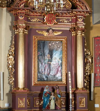 Zdjęcie nr 2: Ołtarz architektoniczny, jednoosiowy, jednokondygnacyjny ze zwieńczeniem. Retabulum osadzone jest na wysokim, zdwojonym, zryzalitowanym uskokowo cokole. Ołtarz jest prostopadłościenny z drewnianą mensą. Część środkową ujmuje para kolumn o żłobkowanych trzonach i korynckich kapitelach, ustawionych na tle zdwojonych pilastrów. Podpory dźwigają wyłamujące się ponad nimi belkowanie o silnie wysuniętym gzymsie. Zwieńczenie ma formę aediculi ujętej parą pilastrów i spływów wolutowych, zamkniętej trójkątnym przyczółkiem. Dodatkowo ujęta jest ona przerwanym, półkolistym przyczółkiem. Płycina antepedium jest w kształcie leżącego prostokąta z płaskorzeźbionym motywem złoconego kielicha eucharystycznego oraz kwiatów lilii skrzyżowanych z włócznią oraz trzciną z gąbką na tle srebrzonych obłoków ujętych promienistą glorią. Płyciny górnego cokołu (predelli) zdobi motyw ostów i cierni. Część środkową ujmuje para ażurowych, akantowych uszaków z motywem tuniki, kolumny biczowania oraz trzciny po lewej stronie i chusty św. Weroniki, drabiny, włóczni i trzciny z gąbką po prawej. U góry, pośrodku znajduje się uskrzydlona główka anielska. Powyżej, w partii belkowania, którego gzyms zdobi kostkowanie, jest umieszczony kartusz herbowy z monogramem IHS. Fryz zdobi stylizowana wić roślinna oraz para uskrzydlonych główek anielskich, natomiast zwieńczenie retabulum m.in. motywy roślinne, rozetki i kampanulle. Szczyt tworzy podtrzymująca krzyż para aniołów o sylwetkach od pasa w dół w formie liści akantu. Na przerwanym przyczółku znajduje się para przyklękających aniołów, ubranych w suknie w kolorach jasnoczerwonym i niebieskim oraz złocone płaszcze, trzymających w dłoniach włócznię i trzcinę z gąbką. Pole w części środkowej ma kształt stojącego prostokąta ujętego profilowaną, złoconą ramą. W środku znajduje się przedstawienie św. Anny nauczającej małą Marię. Pole w zwieńczeniu ma kształt stojącego owalu ujętego złoconą ramą w formie wieńca laurowego. Zawiera wizerunek św. Józefa. 
Struktura retabulum utrzymana jest w odcieniach brązu, partie detalu architektonicznego i ornamentyka są złocone.      
