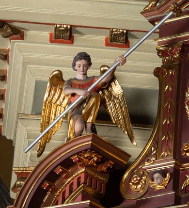 Zdjęcie nr 8: Ołtarz architektoniczny, jednoosiowy, jednokondygnacyjny ze zwieńczeniem. Retabulum osadzone jest na wysokim, zdwojonym, zryzalitowanym uskokowo cokole. Ołtarz jest prostopadłościenny z drewnianą mensą. Część środkową ujmuje para kolumn o żłobkowanych trzonach i korynckich kapitelach, ustawionych na tle zdwojonych pilastrów. Podpory dźwigają wyłamujące się ponad nimi belkowanie o silnie wysuniętym gzymsie. Zwieńczenie ma formę aediculi ujętej parą pilastrów i spływów wolutowych, zamkniętej trójkątnym przyczółkiem. Dodatkowo ujęta jest ona przerwanym, półkolistym przyczółkiem. Płycina antepedium jest w kształcie leżącego prostokąta z płaskorzeźbionym motywem złoconego kielicha eucharystycznego oraz kwiatów lilii skrzyżowanych z włócznią oraz trzciną z gąbką na tle srebrzonych obłoków ujętych promienistą glorią. Płyciny górnego cokołu (predelli) zdobi motyw ostów i cierni. Część środkową ujmuje para ażurowych, akantowych uszaków z motywem tuniki, kolumny biczowania oraz trzciny po lewej stronie i chusty św. Weroniki, drabiny, włóczni i trzciny z gąbką po prawej. U góry, pośrodku znajduje się uskrzydlona główka anielska. Powyżej, w partii belkowania, którego gzyms zdobi kostkowanie, jest umieszczony kartusz herbowy z monogramem IHS. Fryz zdobi stylizowana wić roślinna oraz para uskrzydlonych główek anielskich, natomiast zwieńczenie retabulum m.in. motywy roślinne, rozetki i kampanulle. Szczyt tworzy podtrzymująca krzyż para aniołów o sylwetkach od pasa w dół w formie liści akantu. Na przerwanym przyczółku znajduje się para przyklękających aniołów, ubranych w suknie w kolorach jasnoczerwonym i niebieskim oraz złocone płaszcze, trzymających w dłoniach włócznię i trzcinę z gąbką. Pole w części środkowej ma kształt stojącego prostokąta ujętego profilowaną, złoconą ramą. W środku znajduje się przedstawienie św. Anny nauczającej małą Marię. Pole w zwieńczeniu ma kształt stojącego owalu ujętego złoconą ramą w formie wieńca laurowego. Zawiera wizerunek św. Józefa. 
Struktura retabulum utrzymana jest w odcieniach brązu, partie detalu architektonicznego i ornamentyka są złocone.      
