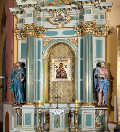 Zdjęcie nr 13: Ołtarz przyścienny, prostopadłościenny, z antepedium, na którym umieszczony jest rzeźbiony monogram Marii; mensa drewniana z kamiennym portatylem. Na mensie znajduje się tabernakulum o kształcie graniastosłupa, z drzwiczkami ozdobionymi rzeźbionym kielichem z hostią. Nastawa ołtarzowa jest architektoniczna, jednoosiowa, jednokondygnacyjna ze zwieńczeniem. Osadzona na podwójnym postumencie, flankowana pilastrami o kompozytowych kapitelach i kanelowanymi kolumnami o kompozytowych kapitelach, które podtrzymują belkowanie. Ponad belkowaniem znajduje się przełamany przyczółek w formie łuku półkolistego, bogato profilowany, ozdobiony ulistnionymi konsolkami i rozetami oraz girlandami z owoców. W partii fryzu kartusz o fantazyjnym wykroju, ujęty wolutami i listkami akantu. Na belkowaniu siedzą po bokach putta, odziane tkaniną na biodrach, a pośrodku znajduje się krzyż osadzony na postumencie z liśćmi. Po obu stronach ołtarza na konsolach o krawędziach ozdobionych ornamentem małżowinowym stoją figury trudnych do identyfikacji świętych, być może apostołów. W centralnej części ołtarza wnęka prostokątna, zamknięta łukiem półkolistym, wypełniona złoconą blachą z rytą ukośną kratką wypełnioną rozetkami. Na blasze zawieszony obraz z przedstawieniem Matki Boskiej Nieustającej Pomocy, który ujęty jest w prostokątną, blaszaną ramę. 

