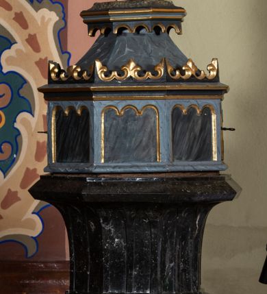 Zdjęcie nr 1: Chrzcielnica na rzucie ośmioboku, trzon i czara również są ośmioboczne. Cokół dwustopniowy, stopnie oddzielone od siebie zaoblonym uskokiem, w górnej części łagodnie przechodzą w trzon. W środkowej partii trzonu spłaszczony ośmioboczny pierścień dekorowany taśmą z płaskorzeźbionymi rozetkami. Czara rozchylająca się ku górze, z profilowaną podstawą, rozczłonkowana ostrołukowatymi płycinami, zakończona profilowanym gzymsem. Ośmioboczna pokrywa o polach z wyciętymi płycinami zamkniętymi potrójnymi łukami półkolistymi jest zwieńczona profilowanym gzymsem z koronką i nakryta daszkiem. Nad nim podstawa ujęta od dołu arkadkowaniem z grupą rzeźbiarską Chrztu w Jordanie. Chrystus stoi w rzece z rękami założonymi na piersi, opasany na biodrach długą białą tkaniną. Przed nim, na skale stoi św. Jan Chrzciciel, ubrany w wielbłądzią skórę z prawą ręką trzymającą naczynie z wodą nad głową Chrystusa, a lewą wyciągniętą do przodu. Nad nim unosi się gołębica Ducha Świętego. 