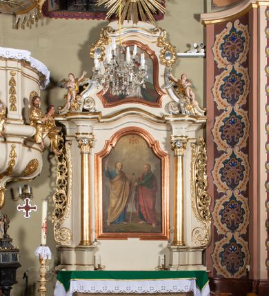 Zdjęcie nr 2: Nastawa ołtarzowa architektoniczna, jednoosiowa, jednokondygnacyjna ze zwieńczeniem. Ołtarz sarkofagowy, wklęsło-wypukły, na cokole, z mensą. Nastawa ujęta parą kolumn o kapitelach kompozytowych, ustawionych na cokołach, dźwigających belkowanie o falistej linii, wyłamane na ich osi, z przerwanym architrawem nad polem środkowym. Na belkowaniu fragmenty przerwanego, falistego przyczółka, dekorowanego rocaille&#039;em, z siedzącymi puttami. Kondygnacja flankowana spływami wolutowymi zdobionymi rocaille&#039;em, opadającymi na cokoły oraz uszami utworzonymi z esowato skręconego akantu. W polu środkowym wnęka w formie stojącego prostokąta zamkniętego łukiem półkolistym nadwieszonym z uskokiem, ujęta profilowaną ramą, z obrazem przedstawiającym św. Piotra i św. Pawła. Zwieńczenie w formie zbliżonej do trapezu, zamkniętego falistym fragmentem gzymsu, flankowane spływami wolutowymi dekorowanymi karbowaną wstęgą oraz rokokowymi kartuszami. W polu obraz św. Heleny w formie zbliżonej do trapezu o falistej linii boków, ujęty profilowaną ramą. Całość zakończona medalionem z monogramem IHS, w otoku z obłoków i dwóch uskrzydlonych główek anielskich, w glorii promienistej. Struktura polichromowana w kolorze beżowym, ze złoconymi kolumnami, ornamentyką i profilami, srebrzonymi detalami i laserowanymi ramami obrazów. 
