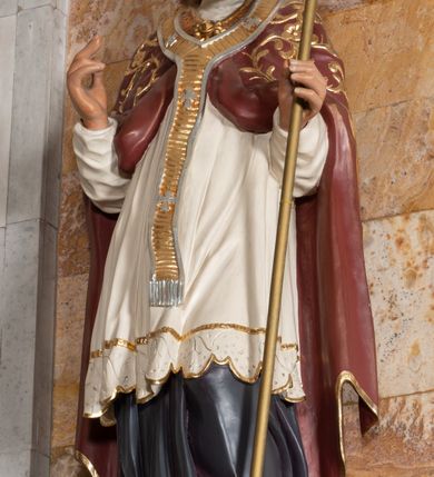 Zdjęcie nr 2: Rzeźba drążona z tyłu stoi na prostokątnej podstawie ustawionej na profilowanej, zwężającej się ku dołowi konsoli przyściennej. Postać biskupa jest ujęta frontalni w nieznacznym kontrapoście z głową lekko skierowaną w prawo. Prawą rękę Augustyn ma uniesioną przed siebie na wysokość piersi w lewej zaś trzyma pastorał o gładkiej, zamkniętej krzywaśni z wpisanym krzyżem równoramiennym. Święty ma pociągłą, wychudzoną twarz o szeroko otwartych oczach, mięsistym nosie i pełnych ustach. Głowę okala broda i lekko kręcone sięgające ramion włosy. Augustyn na głowie ma szkarłatną mitrę zdobiną złotą ornamentyką. Ubrany jest w sutannę, białą komże dekorowaną u spodu szeroką koronką oraz szkarłatną kapę pokrytą złocistym ornamentem i lamowaną złotą tasiemką. Na ramionach dodatkowo ma założony złocony i srebrzony paliusz. Na postumencie widoczny jest podpis: "Ś[WIĘTY] AUGUSTYN".