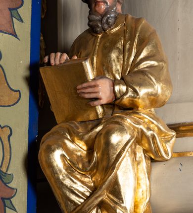 Zdjęcie nr 7: Ambona przyścienna, wisząca, z dostępem przez drzwi w partii zaplecka. Kosz na planie zbliżonym do koła o wklęsło-wypukłym zarysie, na cokole w postaci spłaszczonego wałka, z podwieszeniem w formie zbliżonej do spłaszczonej półkuli, zdobionej rozetami, ujętej lizenami dekorowanymi zwisami, zakończonej szyszką. Ścianki kosza wydzielone pilastrami dźwigającymi belkowanie tworzące parapet. Trzony dekorowane zwisami, ścianki rozetami. Na krawędzi cokołu siedzące figury czterech ewangelistów. Baldachim na planie analogicznym do kosza w formie belkowania z podwieszonym lambrekinem. Na nim woluty tworzące cokół dla wazonu, na którym znajduje się otwarta księga w glorii promienistej. Na księdze napis: „BŁOGOSŁA/WIENI / KTÓRZY / SŁUCHAIĄ / SŁOWA / BOŻEGO, I / STRZEGĄ / GO. / U S(więtego) Łukasza w rozdz(iale) XI wier(sz) [28]”. Na podniebieniu baldachimu gołębica Ducha Świętego w glorii promienistej. Struktura polichromowana w kolorze beżowym, ze złoconymi profilami, ornamentyką i detalami. 