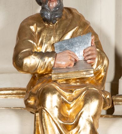 Zdjęcie nr 10: Ambona przyścienna, wisząca, z dostępem przez drzwi w partii zaplecka. Kosz na planie zbliżonym do koła o wklęsło-wypukłym zarysie, na cokole w postaci spłaszczonego wałka, z podwieszeniem w formie zbliżonej do spłaszczonej półkuli, zdobionej rozetami, ujętej lizenami dekorowanymi zwisami, zakończonej szyszką. Ścianki kosza wydzielone pilastrami dźwigającymi belkowanie tworzące parapet. Trzony dekorowane zwisami, ścianki rozetami. Na krawędzi cokołu siedzące figury czterech ewangelistów. Baldachim na planie analogicznym do kosza w formie belkowania z podwieszonym lambrekinem. Na nim woluty tworzące cokół dla wazonu, na którym znajduje się otwarta księga w glorii promienistej. Na księdze napis: „BŁOGOSŁA/WIENI / KTÓRZY / SŁUCHAIĄ / SŁOWA / BOŻEGO, I / STRZEGĄ / GO. / U S(więtego) Łukasza w rozdz(iale) XI wier(sz) [28]”. Na podniebieniu baldachimu gołębica Ducha Świętego w glorii promienistej. Struktura polichromowana w kolorze beżowym, ze złoconymi profilami, ornamentyką i detalami. 