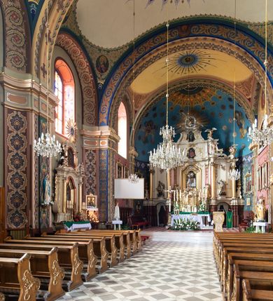 Zdjęcie nr 6: Kościół murowany, tynkowany, na kamiennym podmurowaniu, orientowany, jednonawowy. Prezbiterium prostokątne, krótkie, zamknięte trójbocznie, przy południowej ścianie prostokątna zakrystia z piętrem, z prostokątnym aneksem od zachodu. Nawa główna szersza od prezbiterium, na rzucie prostokąta, od zachodu przylega prostokątny przedsionek z wieżą na planie kwadratu. Wnętrze podzielone na cztery prostokątne przęsła i absydę, wydzielone arkadami, z gurtami spływającymi na zwielokrotnione pilastry. Każde przęsło nakryte sklepieniem o zaokrąglonych narożach. Łuk tęczowy półkolisty. W zachodniej części parapet chóru muzycznego wsparty na dwóch filarach i dwóch półfilarach, tworzących trzy arkady. Fasada trójosiowa, z wbudowaną wieżą, ujętą spłaszczonymi spływami zakończonymi cokołami z figurami. Osie wydzielone lizenami, podtrzymującymi profilowany gzyms, pod nim malowany fryz z dekoracją roślinną. Na osi portal w formie stojącego prostokąta zamkniętego łukiem odcinkowym, ujęty opaską tynkową, zakończoną kluczem. Drzwi drewniane, dwuskrzydłowe. Nad portalem fragment profilowanego gzymsu z daszkiem okapowym. Powyżej, na osi okno w formie stojącego prostokąta zamkniętego łukiem odcinkowym, w profilowanej opasce tynkowej, ujętej malowaną dekoracją geometryczną. Wieża dwukondygnacyjna, flankowana w narożach lizenami podtrzymującymi profilowany gzyms wieńczący. Na ścianie frontowej dwa okna na każdej kondygnacji, w formie stojącego prostokąta zamkniętego łukiem odcinkowym, w profilowanej opasce tynkowej, otoczonej malowaną dekoracją geometryczną, zwieńczone tarczą zegarową. Na pozostałych trzech ścianach wieży po jednym analogicznym oknie w drugiej kondygnacji i tarczy zegarowej. Elewacje północna i południowa artykułowane lizenami podtrzymującymi profilowany gzyms, z dekoracyjnym fryzem poniżej. Okna w formie stojącego prostokąta zamkniętego łukiem odcinkowym, w profilowanej opasce tynkowej z kluczem, ujętej malowaną dekoracją geometryczną: cztery w północnej i trzy w południowej. W zakrystii jedno prostokątne okno od południa i dwa w każdej kondygnacji od wschodu. Nawa główna i prezbiterium nakryte osobnymi dachami dwuspadowymi. Na ich połączeniu wieżyczka na sygnaturkę z latarnią, zwieńczona hełmem baniastym z krzyżem. Wieża nakryta hełmem baniastym zakończonym kulą z krzyżem. Zakrystia przykryta dachem trójspadowym, a aneks czterospadowym. 