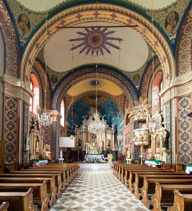 Zdjęcie nr 24: Kościół murowany, tynkowany, na kamiennym podmurowaniu, orientowany, jednonawowy. Prezbiterium prostokątne, krótkie, zamknięte trójbocznie, przy południowej ścianie prostokątna zakrystia z piętrem, z prostokątnym aneksem od zachodu. Nawa główna szersza od prezbiterium, na rzucie prostokąta, od zachodu przylega prostokątny przedsionek z wieżą na planie kwadratu. Wnętrze podzielone na cztery prostokątne przęsła i absydę, wydzielone arkadami, z gurtami spływającymi na zwielokrotnione pilastry. Każde przęsło nakryte sklepieniem o zaokrąglonych narożach. Łuk tęczowy półkolisty. W zachodniej części parapet chóru muzycznego wsparty na dwóch filarach i dwóch półfilarach, tworzących trzy arkady. Fasada trójosiowa, z wbudowaną wieżą, ujętą spłaszczonymi spływami zakończonymi cokołami z figurami. Osie wydzielone lizenami, podtrzymującymi profilowany gzyms, pod nim malowany fryz z dekoracją roślinną. Na osi portal w formie stojącego prostokąta zamkniętego łukiem odcinkowym, ujęty opaską tynkową, zakończoną kluczem. Drzwi drewniane, dwuskrzydłowe. Nad portalem fragment profilowanego gzymsu z daszkiem okapowym. Powyżej, na osi okno w formie stojącego prostokąta zamkniętego łukiem odcinkowym, w profilowanej opasce tynkowej, ujętej malowaną dekoracją geometryczną. Wieża dwukondygnacyjna, flankowana w narożach lizenami podtrzymującymi profilowany gzyms wieńczący. Na ścianie frontowej dwa okna na każdej kondygnacji, w formie stojącego prostokąta zamkniętego łukiem odcinkowym, w profilowanej opasce tynkowej, otoczonej malowaną dekoracją geometryczną, zwieńczone tarczą zegarową. Na pozostałych trzech ścianach wieży po jednym analogicznym oknie w drugiej kondygnacji i tarczy zegarowej. Elewacje północna i południowa artykułowane lizenami podtrzymującymi profilowany gzyms, z dekoracyjnym fryzem poniżej. Okna w formie stojącego prostokąta zamkniętego łukiem odcinkowym, w profilowanej opasce tynkowej z kluczem, ujętej malowaną dekoracją geometryczną: cztery w północnej i trzy w południowej. W zakrystii jedno prostokątne okno od południa i dwa w każdej kondygnacji od wschodu. Nawa główna i prezbiterium nakryte osobnymi dachami dwuspadowymi. Na ich połączeniu wieżyczka na sygnaturkę z latarnią, zwieńczona hełmem baniastym z krzyżem. Wieża nakryta hełmem baniastym zakończonym kulą z krzyżem. Zakrystia przykryta dachem trójspadowym, a aneks czterospadowym. 