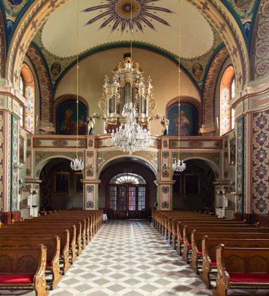 Zdjęcie nr 9: Kościół murowany, tynkowany, na kamiennym podmurowaniu, orientowany, jednonawowy. Prezbiterium prostokątne, krótkie, zamknięte trójbocznie, przy południowej ścianie prostokątna zakrystia z piętrem, z prostokątnym aneksem od zachodu. Nawa główna szersza od prezbiterium, na rzucie prostokąta, od zachodu przylega prostokątny przedsionek z wieżą na planie kwadratu. Wnętrze podzielone na cztery prostokątne przęsła i absydę, wydzielone arkadami, z gurtami spływającymi na zwielokrotnione pilastry. Każde przęsło nakryte sklepieniem o zaokrąglonych narożach. Łuk tęczowy półkolisty. W zachodniej części parapet chóru muzycznego wsparty na dwóch filarach i dwóch półfilarach, tworzących trzy arkady. Fasada trójosiowa, z wbudowaną wieżą, ujętą spłaszczonymi spływami zakończonymi cokołami z figurami. Osie wydzielone lizenami, podtrzymującymi profilowany gzyms, pod nim malowany fryz z dekoracją roślinną. Na osi portal w formie stojącego prostokąta zamkniętego łukiem odcinkowym, ujęty opaską tynkową, zakończoną kluczem. Drzwi drewniane, dwuskrzydłowe. Nad portalem fragment profilowanego gzymsu z daszkiem okapowym. Powyżej, na osi okno w formie stojącego prostokąta zamkniętego łukiem odcinkowym, w profilowanej opasce tynkowej, ujętej malowaną dekoracją geometryczną. Wieża dwukondygnacyjna, flankowana w narożach lizenami podtrzymującymi profilowany gzyms wieńczący. Na ścianie frontowej dwa okna na każdej kondygnacji, w formie stojącego prostokąta zamkniętego łukiem odcinkowym, w profilowanej opasce tynkowej, otoczonej malowaną dekoracją geometryczną, zwieńczone tarczą zegarową. Na pozostałych trzech ścianach wieży po jednym analogicznym oknie w drugiej kondygnacji i tarczy zegarowej. Elewacje północna i południowa artykułowane lizenami podtrzymującymi profilowany gzyms, z dekoracyjnym fryzem poniżej. Okna w formie stojącego prostokąta zamkniętego łukiem odcinkowym, w profilowanej opasce tynkowej z kluczem, ujętej malowaną dekoracją geometryczną: cztery w północnej i trzy w południowej. W zakrystii jedno prostokątne okno od południa i dwa w każdej kondygnacji od wschodu. Nawa główna i prezbiterium nakryte osobnymi dachami dwuspadowymi. Na ich połączeniu wieżyczka na sygnaturkę z latarnią, zwieńczona hełmem baniastym z krzyżem. Wieża nakryta hełmem baniastym zakończonym kulą z krzyżem. Zakrystia przykryta dachem trójspadowym, a aneks czterospadowym. 