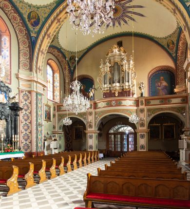 Zdjęcie nr 15: Kościół murowany, tynkowany, na kamiennym podmurowaniu, orientowany, jednonawowy. Prezbiterium prostokątne, krótkie, zamknięte trójbocznie, przy południowej ścianie prostokątna zakrystia z piętrem, z prostokątnym aneksem od zachodu. Nawa główna szersza od prezbiterium, na rzucie prostokąta, od zachodu przylega prostokątny przedsionek z wieżą na planie kwadratu. Wnętrze podzielone na cztery prostokątne przęsła i absydę, wydzielone arkadami, z gurtami spływającymi na zwielokrotnione pilastry. Każde przęsło nakryte sklepieniem o zaokrąglonych narożach. Łuk tęczowy półkolisty. W zachodniej części parapet chóru muzycznego wsparty na dwóch filarach i dwóch półfilarach, tworzących trzy arkady. Fasada trójosiowa, z wbudowaną wieżą, ujętą spłaszczonymi spływami zakończonymi cokołami z figurami. Osie wydzielone lizenami, podtrzymującymi profilowany gzyms, pod nim malowany fryz z dekoracją roślinną. Na osi portal w formie stojącego prostokąta zamkniętego łukiem odcinkowym, ujęty opaską tynkową, zakończoną kluczem. Drzwi drewniane, dwuskrzydłowe. Nad portalem fragment profilowanego gzymsu z daszkiem okapowym. Powyżej, na osi okno w formie stojącego prostokąta zamkniętego łukiem odcinkowym, w profilowanej opasce tynkowej, ujętej malowaną dekoracją geometryczną. Wieża dwukondygnacyjna, flankowana w narożach lizenami podtrzymującymi profilowany gzyms wieńczący. Na ścianie frontowej dwa okna na każdej kondygnacji, w formie stojącego prostokąta zamkniętego łukiem odcinkowym, w profilowanej opasce tynkowej, otoczonej malowaną dekoracją geometryczną, zwieńczone tarczą zegarową. Na pozostałych trzech ścianach wieży po jednym analogicznym oknie w drugiej kondygnacji i tarczy zegarowej. Elewacje północna i południowa artykułowane lizenami podtrzymującymi profilowany gzyms, z dekoracyjnym fryzem poniżej. Okna w formie stojącego prostokąta zamkniętego łukiem odcinkowym, w profilowanej opasce tynkowej z kluczem, ujętej malowaną dekoracją geometryczną: cztery w północnej i trzy w południowej. W zakrystii jedno prostokątne okno od południa i dwa w każdej kondygnacji od wschodu. Nawa główna i prezbiterium nakryte osobnymi dachami dwuspadowymi. Na ich połączeniu wieżyczka na sygnaturkę z latarnią, zwieńczona hełmem baniastym z krzyżem. Wieża nakryta hełmem baniastym zakończonym kulą z krzyżem. Zakrystia przykryta dachem trójspadowym, a aneks czterospadowym. 