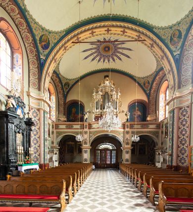 Zdjęcie nr 14: Kościół murowany, tynkowany, na kamiennym podmurowaniu, orientowany, jednonawowy. Prezbiterium prostokątne, krótkie, zamknięte trójbocznie, przy południowej ścianie prostokątna zakrystia z piętrem, z prostokątnym aneksem od zachodu. Nawa główna szersza od prezbiterium, na rzucie prostokąta, od zachodu przylega prostokątny przedsionek z wieżą na planie kwadratu. Wnętrze podzielone na cztery prostokątne przęsła i absydę, wydzielone arkadami, z gurtami spływającymi na zwielokrotnione pilastry. Każde przęsło nakryte sklepieniem o zaokrąglonych narożach. Łuk tęczowy półkolisty. W zachodniej części parapet chóru muzycznego wsparty na dwóch filarach i dwóch półfilarach, tworzących trzy arkady. Fasada trójosiowa, z wbudowaną wieżą, ujętą spłaszczonymi spływami zakończonymi cokołami z figurami. Osie wydzielone lizenami, podtrzymującymi profilowany gzyms, pod nim malowany fryz z dekoracją roślinną. Na osi portal w formie stojącego prostokąta zamkniętego łukiem odcinkowym, ujęty opaską tynkową, zakończoną kluczem. Drzwi drewniane, dwuskrzydłowe. Nad portalem fragment profilowanego gzymsu z daszkiem okapowym. Powyżej, na osi okno w formie stojącego prostokąta zamkniętego łukiem odcinkowym, w profilowanej opasce tynkowej, ujętej malowaną dekoracją geometryczną. Wieża dwukondygnacyjna, flankowana w narożach lizenami podtrzymującymi profilowany gzyms wieńczący. Na ścianie frontowej dwa okna na każdej kondygnacji, w formie stojącego prostokąta zamkniętego łukiem odcinkowym, w profilowanej opasce tynkowej, otoczonej malowaną dekoracją geometryczną, zwieńczone tarczą zegarową. Na pozostałych trzech ścianach wieży po jednym analogicznym oknie w drugiej kondygnacji i tarczy zegarowej. Elewacje północna i południowa artykułowane lizenami podtrzymującymi profilowany gzyms, z dekoracyjnym fryzem poniżej. Okna w formie stojącego prostokąta zamkniętego łukiem odcinkowym, w profilowanej opasce tynkowej z kluczem, ujętej malowaną dekoracją geometryczną: cztery w północnej i trzy w południowej. W zakrystii jedno prostokątne okno od południa i dwa w każdej kondygnacji od wschodu. Nawa główna i prezbiterium nakryte osobnymi dachami dwuspadowymi. Na ich połączeniu wieżyczka na sygnaturkę z latarnią, zwieńczona hełmem baniastym z krzyżem. Wieża nakryta hełmem baniastym zakończonym kulą z krzyżem. Zakrystia przykryta dachem trójspadowym, a aneks czterospadowym. 