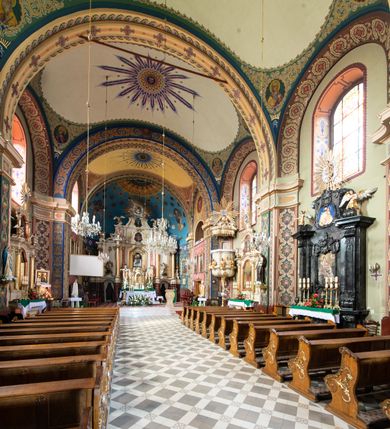 Zdjęcie nr 7: Kościół murowany, tynkowany, na kamiennym podmurowaniu, orientowany, jednonawowy. Prezbiterium prostokątne, krótkie, zamknięte trójbocznie, przy południowej ścianie prostokątna zakrystia z piętrem, z prostokątnym aneksem od zachodu. Nawa główna szersza od prezbiterium, na rzucie prostokąta, od zachodu przylega prostokątny przedsionek z wieżą na planie kwadratu. Wnętrze podzielone na cztery prostokątne przęsła i absydę, wydzielone arkadami, z gurtami spływającymi na zwielokrotnione pilastry. Każde przęsło nakryte sklepieniem o zaokrąglonych narożach. Łuk tęczowy półkolisty. W zachodniej części parapet chóru muzycznego wsparty na dwóch filarach i dwóch półfilarach, tworzących trzy arkady. Fasada trójosiowa, z wbudowaną wieżą, ujętą spłaszczonymi spływami zakończonymi cokołami z figurami. Osie wydzielone lizenami, podtrzymującymi profilowany gzyms, pod nim malowany fryz z dekoracją roślinną. Na osi portal w formie stojącego prostokąta zamkniętego łukiem odcinkowym, ujęty opaską tynkową, zakończoną kluczem. Drzwi drewniane, dwuskrzydłowe. Nad portalem fragment profilowanego gzymsu z daszkiem okapowym. Powyżej, na osi okno w formie stojącego prostokąta zamkniętego łukiem odcinkowym, w profilowanej opasce tynkowej, ujętej malowaną dekoracją geometryczną. Wieża dwukondygnacyjna, flankowana w narożach lizenami podtrzymującymi profilowany gzyms wieńczący. Na ścianie frontowej dwa okna na każdej kondygnacji, w formie stojącego prostokąta zamkniętego łukiem odcinkowym, w profilowanej opasce tynkowej, otoczonej malowaną dekoracją geometryczną, zwieńczone tarczą zegarową. Na pozostałych trzech ścianach wieży po jednym analogicznym oknie w drugiej kondygnacji i tarczy zegarowej. Elewacje północna i południowa artykułowane lizenami podtrzymującymi profilowany gzyms, z dekoracyjnym fryzem poniżej. Okna w formie stojącego prostokąta zamkniętego łukiem odcinkowym, w profilowanej opasce tynkowej z kluczem, ujętej malowaną dekoracją geometryczną: cztery w północnej i trzy w południowej. W zakrystii jedno prostokątne okno od południa i dwa w każdej kondygnacji od wschodu. Nawa główna i prezbiterium nakryte osobnymi dachami dwuspadowymi. Na ich połączeniu wieżyczka na sygnaturkę z latarnią, zwieńczona hełmem baniastym z krzyżem. Wieża nakryta hełmem baniastym zakończonym kulą z krzyżem. Zakrystia przykryta dachem trójspadowym, a aneks czterospadowym. 