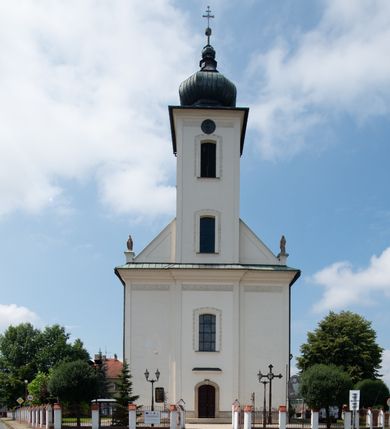 Zdjęcie nr 2: Kościół murowany, tynkowany, na kamiennym podmurowaniu, orientowany, jednonawowy. Prezbiterium prostokątne, krótkie, zamknięte trójbocznie, przy południowej ścianie prostokątna zakrystia z piętrem, z prostokątnym aneksem od zachodu. Nawa główna szersza od prezbiterium, na rzucie prostokąta, od zachodu przylega prostokątny przedsionek z wieżą na planie kwadratu. Wnętrze podzielone na cztery prostokątne przęsła i absydę, wydzielone arkadami, z gurtami spływającymi na zwielokrotnione pilastry. Każde przęsło nakryte sklepieniem o zaokrąglonych narożach. Łuk tęczowy półkolisty. W zachodniej części parapet chóru muzycznego wsparty na dwóch filarach i dwóch półfilarach, tworzących trzy arkady. Fasada trójosiowa, z wbudowaną wieżą, ujętą spłaszczonymi spływami zakończonymi cokołami z figurami. Osie wydzielone lizenami, podtrzymującymi profilowany gzyms, pod nim malowany fryz z dekoracją roślinną. Na osi portal w formie stojącego prostokąta zamkniętego łukiem odcinkowym, ujęty opaską tynkową, zakończoną kluczem. Drzwi drewniane, dwuskrzydłowe. Nad portalem fragment profilowanego gzymsu z daszkiem okapowym. Powyżej, na osi okno w formie stojącego prostokąta zamkniętego łukiem odcinkowym, w profilowanej opasce tynkowej, ujętej malowaną dekoracją geometryczną. Wieża dwukondygnacyjna, flankowana w narożach lizenami podtrzymującymi profilowany gzyms wieńczący. Na ścianie frontowej dwa okna na każdej kondygnacji, w formie stojącego prostokąta zamkniętego łukiem odcinkowym, w profilowanej opasce tynkowej, otoczonej malowaną dekoracją geometryczną, zwieńczone tarczą zegarową. Na pozostałych trzech ścianach wieży po jednym analogicznym oknie w drugiej kondygnacji i tarczy zegarowej. Elewacje północna i południowa artykułowane lizenami podtrzymującymi profilowany gzyms, z dekoracyjnym fryzem poniżej. Okna w formie stojącego prostokąta zamkniętego łukiem odcinkowym, w profilowanej opasce tynkowej z kluczem, ujętej malowaną dekoracją geometryczną: cztery w północnej i trzy w południowej. W zakrystii jedno prostokątne okno od południa i dwa w każdej kondygnacji od wschodu. Nawa główna i prezbiterium nakryte osobnymi dachami dwuspadowymi. Na ich połączeniu wieżyczka na sygnaturkę z latarnią, zwieńczona hełmem baniastym z krzyżem. Wieża nakryta hełmem baniastym zakończonym kulą z krzyżem. Zakrystia przykryta dachem trójspadowym, a aneks czterospadowym. 