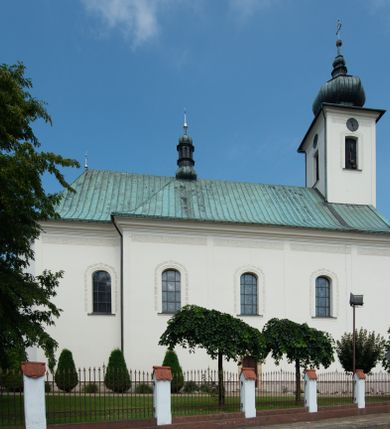 Zdjęcie nr 20: Kościół murowany, tynkowany, na kamiennym podmurowaniu, orientowany, jednonawowy. Prezbiterium prostokątne, krótkie, zamknięte trójbocznie, przy południowej ścianie prostokątna zakrystia z piętrem, z prostokątnym aneksem od zachodu. Nawa główna szersza od prezbiterium, na rzucie prostokąta, od zachodu przylega prostokątny przedsionek z wieżą na planie kwadratu. Wnętrze podzielone na cztery prostokątne przęsła i absydę, wydzielone arkadami, z gurtami spływającymi na zwielokrotnione pilastry. Każde przęsło nakryte sklepieniem o zaokrąglonych narożach. Łuk tęczowy półkolisty. W zachodniej części parapet chóru muzycznego wsparty na dwóch filarach i dwóch półfilarach, tworzących trzy arkady. Fasada trójosiowa, z wbudowaną wieżą, ujętą spłaszczonymi spływami zakończonymi cokołami z figurami. Osie wydzielone lizenami, podtrzymującymi profilowany gzyms, pod nim malowany fryz z dekoracją roślinną. Na osi portal w formie stojącego prostokąta zamkniętego łukiem odcinkowym, ujęty opaską tynkową, zakończoną kluczem. Drzwi drewniane, dwuskrzydłowe. Nad portalem fragment profilowanego gzymsu z daszkiem okapowym. Powyżej, na osi okno w formie stojącego prostokąta zamkniętego łukiem odcinkowym, w profilowanej opasce tynkowej, ujętej malowaną dekoracją geometryczną. Wieża dwukondygnacyjna, flankowana w narożach lizenami podtrzymującymi profilowany gzyms wieńczący. Na ścianie frontowej dwa okna na każdej kondygnacji, w formie stojącego prostokąta zamkniętego łukiem odcinkowym, w profilowanej opasce tynkowej, otoczonej malowaną dekoracją geometryczną, zwieńczone tarczą zegarową. Na pozostałych trzech ścianach wieży po jednym analogicznym oknie w drugiej kondygnacji i tarczy zegarowej. Elewacje północna i południowa artykułowane lizenami podtrzymującymi profilowany gzyms, z dekoracyjnym fryzem poniżej. Okna w formie stojącego prostokąta zamkniętego łukiem odcinkowym, w profilowanej opasce tynkowej z kluczem, ujętej malowaną dekoracją geometryczną: cztery w północnej i trzy w południowej. W zakrystii jedno prostokątne okno od południa i dwa w każdej kondygnacji od wschodu. Nawa główna i prezbiterium nakryte osobnymi dachami dwuspadowymi. Na ich połączeniu wieżyczka na sygnaturkę z latarnią, zwieńczona hełmem baniastym z krzyżem. Wieża nakryta hełmem baniastym zakończonym kulą z krzyżem. Zakrystia przykryta dachem trójspadowym, a aneks czterospadowym. 