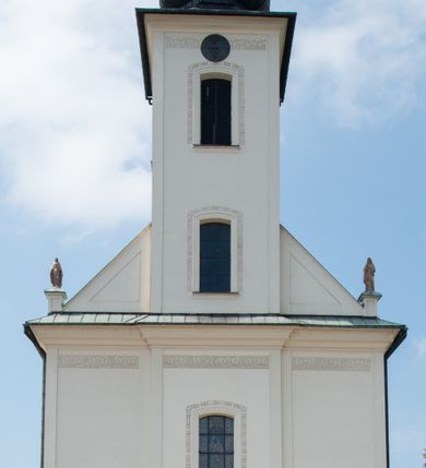 Zdjęcie nr 18: Kościół murowany, tynkowany, na kamiennym podmurowaniu, orientowany, jednonawowy. Prezbiterium prostokątne, krótkie, zamknięte trójbocznie, przy południowej ścianie prostokątna zakrystia z piętrem, z prostokątnym aneksem od zachodu. Nawa główna szersza od prezbiterium, na rzucie prostokąta, od zachodu przylega prostokątny przedsionek z wieżą na planie kwadratu. Wnętrze podzielone na cztery prostokątne przęsła i absydę, wydzielone arkadami, z gurtami spływającymi na zwielokrotnione pilastry. Każde przęsło nakryte sklepieniem o zaokrąglonych narożach. Łuk tęczowy półkolisty. W zachodniej części parapet chóru muzycznego wsparty na dwóch filarach i dwóch półfilarach, tworzących trzy arkady. Fasada trójosiowa, z wbudowaną wieżą, ujętą spłaszczonymi spływami zakończonymi cokołami z figurami. Osie wydzielone lizenami, podtrzymującymi profilowany gzyms, pod nim malowany fryz z dekoracją roślinną. Na osi portal w formie stojącego prostokąta zamkniętego łukiem odcinkowym, ujęty opaską tynkową, zakończoną kluczem. Drzwi drewniane, dwuskrzydłowe. Nad portalem fragment profilowanego gzymsu z daszkiem okapowym. Powyżej, na osi okno w formie stojącego prostokąta zamkniętego łukiem odcinkowym, w profilowanej opasce tynkowej, ujętej malowaną dekoracją geometryczną. Wieża dwukondygnacyjna, flankowana w narożach lizenami podtrzymującymi profilowany gzyms wieńczący. Na ścianie frontowej dwa okna na każdej kondygnacji, w formie stojącego prostokąta zamkniętego łukiem odcinkowym, w profilowanej opasce tynkowej, otoczonej malowaną dekoracją geometryczną, zwieńczone tarczą zegarową. Na pozostałych trzech ścianach wieży po jednym analogicznym oknie w drugiej kondygnacji i tarczy zegarowej. Elewacje północna i południowa artykułowane lizenami podtrzymującymi profilowany gzyms, z dekoracyjnym fryzem poniżej. Okna w formie stojącego prostokąta zamkniętego łukiem odcinkowym, w profilowanej opasce tynkowej z kluczem, ujętej malowaną dekoracją geometryczną: cztery w północnej i trzy w południowej. W zakrystii jedno prostokątne okno od południa i dwa w każdej kondygnacji od wschodu. Nawa główna i prezbiterium nakryte osobnymi dachami dwuspadowymi. Na ich połączeniu wieżyczka na sygnaturkę z latarnią, zwieńczona hełmem baniastym z krzyżem. Wieża nakryta hełmem baniastym zakończonym kulą z krzyżem. Zakrystia przykryta dachem trójspadowym, a aneks czterospadowym. 