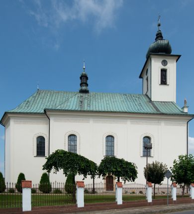 Zdjęcie nr 22: Kościół murowany, tynkowany, na kamiennym podmurowaniu, orientowany, jednonawowy. Prezbiterium prostokątne, krótkie, zamknięte trójbocznie, przy południowej ścianie prostokątna zakrystia z piętrem, z prostokątnym aneksem od zachodu. Nawa główna szersza od prezbiterium, na rzucie prostokąta, od zachodu przylega prostokątny przedsionek z wieżą na planie kwadratu. Wnętrze podzielone na cztery prostokątne przęsła i absydę, wydzielone arkadami, z gurtami spływającymi na zwielokrotnione pilastry. Każde przęsło nakryte sklepieniem o zaokrąglonych narożach. Łuk tęczowy półkolisty. W zachodniej części parapet chóru muzycznego wsparty na dwóch filarach i dwóch półfilarach, tworzących trzy arkady. Fasada trójosiowa, z wbudowaną wieżą, ujętą spłaszczonymi spływami zakończonymi cokołami z figurami. Osie wydzielone lizenami, podtrzymującymi profilowany gzyms, pod nim malowany fryz z dekoracją roślinną. Na osi portal w formie stojącego prostokąta zamkniętego łukiem odcinkowym, ujęty opaską tynkową, zakończoną kluczem. Drzwi drewniane, dwuskrzydłowe. Nad portalem fragment profilowanego gzymsu z daszkiem okapowym. Powyżej, na osi okno w formie stojącego prostokąta zamkniętego łukiem odcinkowym, w profilowanej opasce tynkowej, ujętej malowaną dekoracją geometryczną. Wieża dwukondygnacyjna, flankowana w narożach lizenami podtrzymującymi profilowany gzyms wieńczący. Na ścianie frontowej dwa okna na każdej kondygnacji, w formie stojącego prostokąta zamkniętego łukiem odcinkowym, w profilowanej opasce tynkowej, otoczonej malowaną dekoracją geometryczną, zwieńczone tarczą zegarową. Na pozostałych trzech ścianach wieży po jednym analogicznym oknie w drugiej kondygnacji i tarczy zegarowej. Elewacje północna i południowa artykułowane lizenami podtrzymującymi profilowany gzyms, z dekoracyjnym fryzem poniżej. Okna w formie stojącego prostokąta zamkniętego łukiem odcinkowym, w profilowanej opasce tynkowej z kluczem, ujętej malowaną dekoracją geometryczną: cztery w północnej i trzy w południowej. W zakrystii jedno prostokątne okno od południa i dwa w każdej kondygnacji od wschodu. Nawa główna i prezbiterium nakryte osobnymi dachami dwuspadowymi. Na ich połączeniu wieżyczka na sygnaturkę z latarnią, zwieńczona hełmem baniastym z krzyżem. Wieża nakryta hełmem baniastym zakończonym kulą z krzyżem. Zakrystia przykryta dachem trójspadowym, a aneks czterospadowym. 