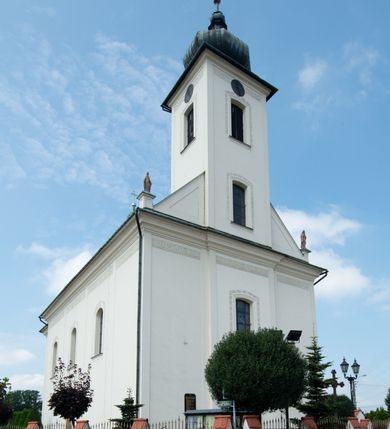 Zdjęcie nr 19: Kościół murowany, tynkowany, na kamiennym podmurowaniu, orientowany, jednonawowy. Prezbiterium prostokątne, krótkie, zamknięte trójbocznie, przy południowej ścianie prostokątna zakrystia z piętrem, z prostokątnym aneksem od zachodu. Nawa główna szersza od prezbiterium, na rzucie prostokąta, od zachodu przylega prostokątny przedsionek z wieżą na planie kwadratu. Wnętrze podzielone na cztery prostokątne przęsła i absydę, wydzielone arkadami, z gurtami spływającymi na zwielokrotnione pilastry. Każde przęsło nakryte sklepieniem o zaokrąglonych narożach. Łuk tęczowy półkolisty. W zachodniej części parapet chóru muzycznego wsparty na dwóch filarach i dwóch półfilarach, tworzących trzy arkady. Fasada trójosiowa, z wbudowaną wieżą, ujętą spłaszczonymi spływami zakończonymi cokołami z figurami. Osie wydzielone lizenami, podtrzymującymi profilowany gzyms, pod nim malowany fryz z dekoracją roślinną. Na osi portal w formie stojącego prostokąta zamkniętego łukiem odcinkowym, ujęty opaską tynkową, zakończoną kluczem. Drzwi drewniane, dwuskrzydłowe. Nad portalem fragment profilowanego gzymsu z daszkiem okapowym. Powyżej, na osi okno w formie stojącego prostokąta zamkniętego łukiem odcinkowym, w profilowanej opasce tynkowej, ujętej malowaną dekoracją geometryczną. Wieża dwukondygnacyjna, flankowana w narożach lizenami podtrzymującymi profilowany gzyms wieńczący. Na ścianie frontowej dwa okna na każdej kondygnacji, w formie stojącego prostokąta zamkniętego łukiem odcinkowym, w profilowanej opasce tynkowej, otoczonej malowaną dekoracją geometryczną, zwieńczone tarczą zegarową. Na pozostałych trzech ścianach wieży po jednym analogicznym oknie w drugiej kondygnacji i tarczy zegarowej. Elewacje północna i południowa artykułowane lizenami podtrzymującymi profilowany gzyms, z dekoracyjnym fryzem poniżej. Okna w formie stojącego prostokąta zamkniętego łukiem odcinkowym, w profilowanej opasce tynkowej z kluczem, ujętej malowaną dekoracją geometryczną: cztery w północnej i trzy w południowej. W zakrystii jedno prostokątne okno od południa i dwa w każdej kondygnacji od wschodu. Nawa główna i prezbiterium nakryte osobnymi dachami dwuspadowymi. Na ich połączeniu wieżyczka na sygnaturkę z latarnią, zwieńczona hełmem baniastym z krzyżem. Wieża nakryta hełmem baniastym zakończonym kulą z krzyżem. Zakrystia przykryta dachem trójspadowym, a aneks czterospadowym. 